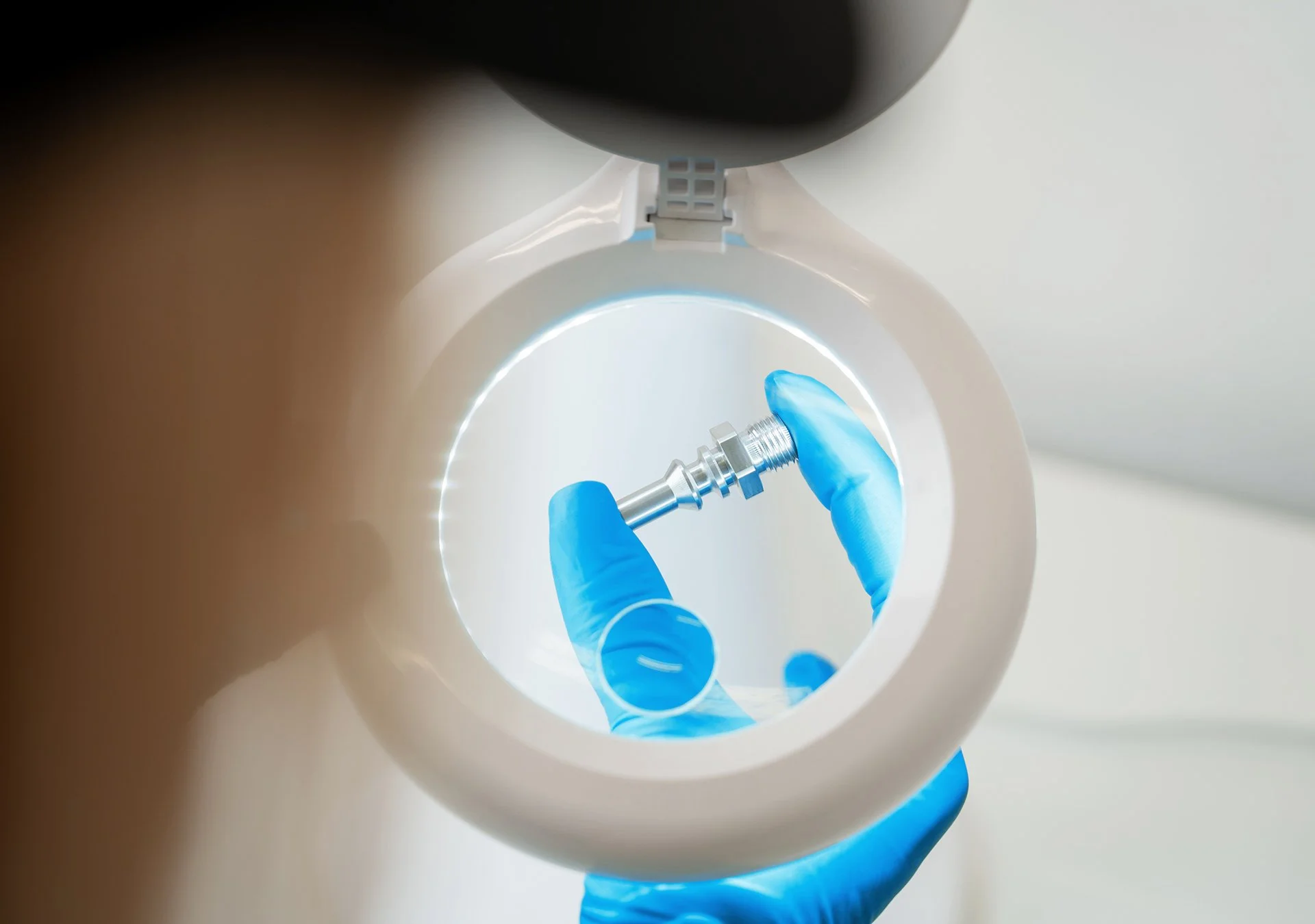 En person i blå handskar hanterar en svarvad metalldel i ett kliniskt laboratorium.