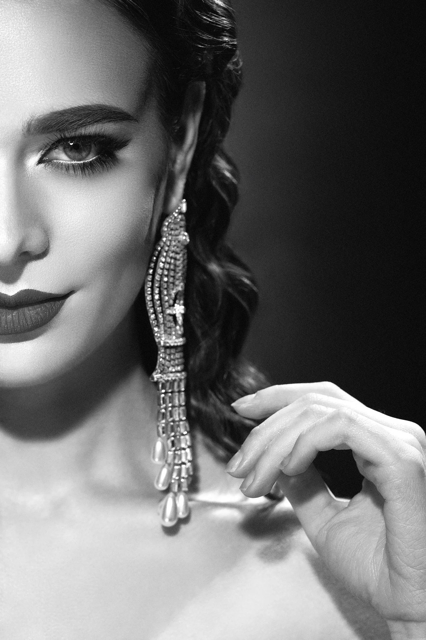 Cropped black-and-white glamour portrait featuring dramatic eye makeup, dark lipstick and a long crystal statement earring.