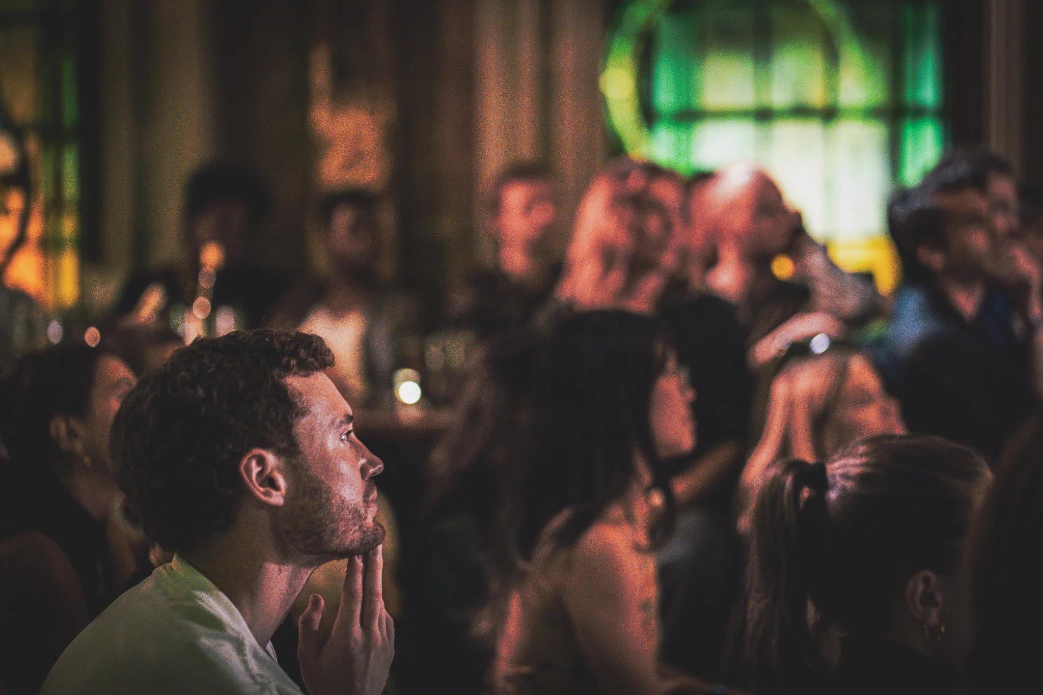 Audience members attentively listening at a RAW uncensored storytelling night with stained glass windows in the background.