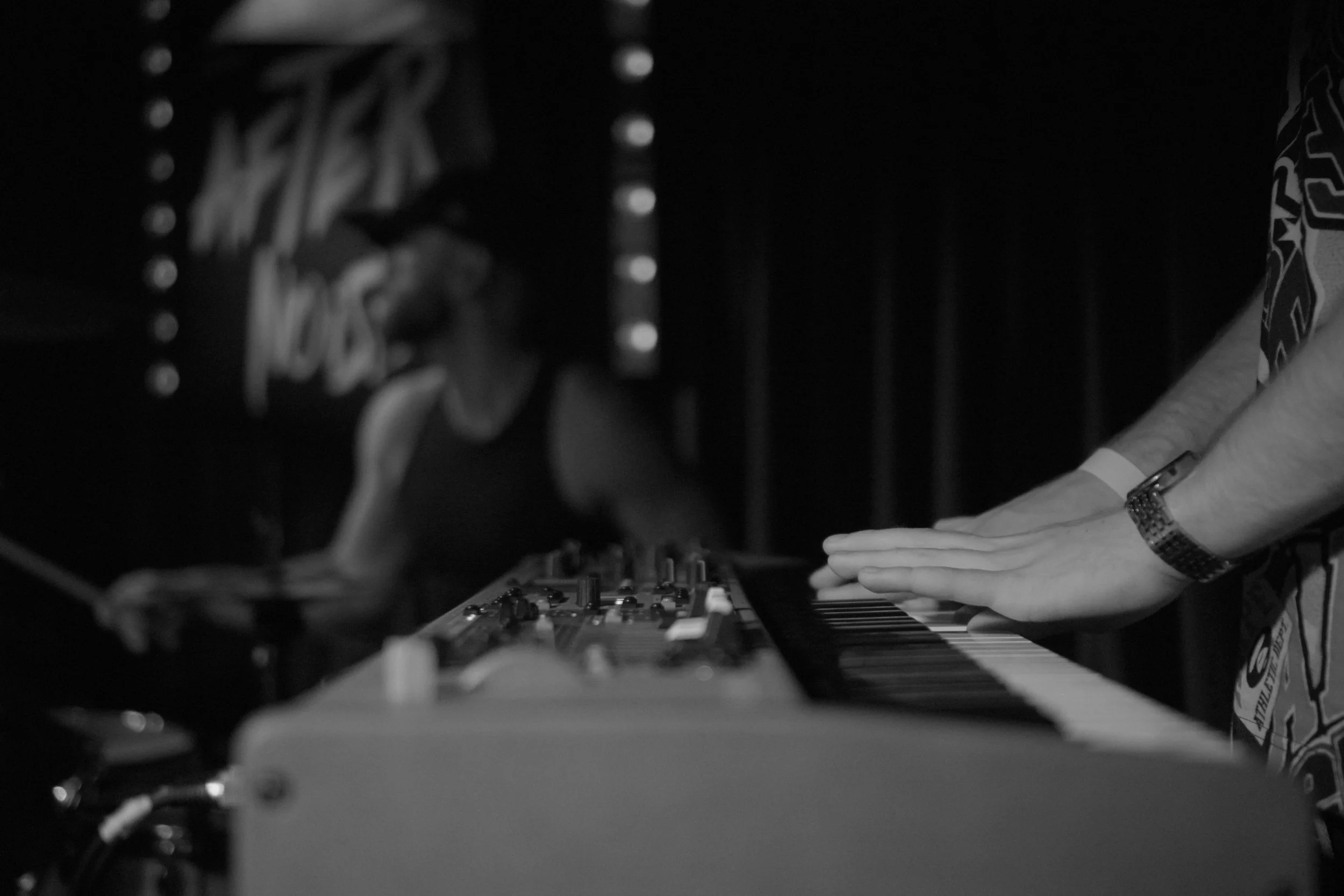 Person playing a keyboard and DJing in a dark room with DJ equipment at a RAW Afternoise open jam, music improv night.