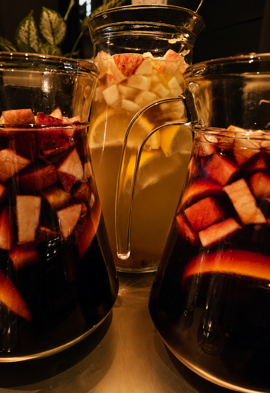Three glass pitchers filled with chopped fruits and sangria, with a leafy plant in the background at a What Does Not culture club, part of learning a language in London through the culture. 