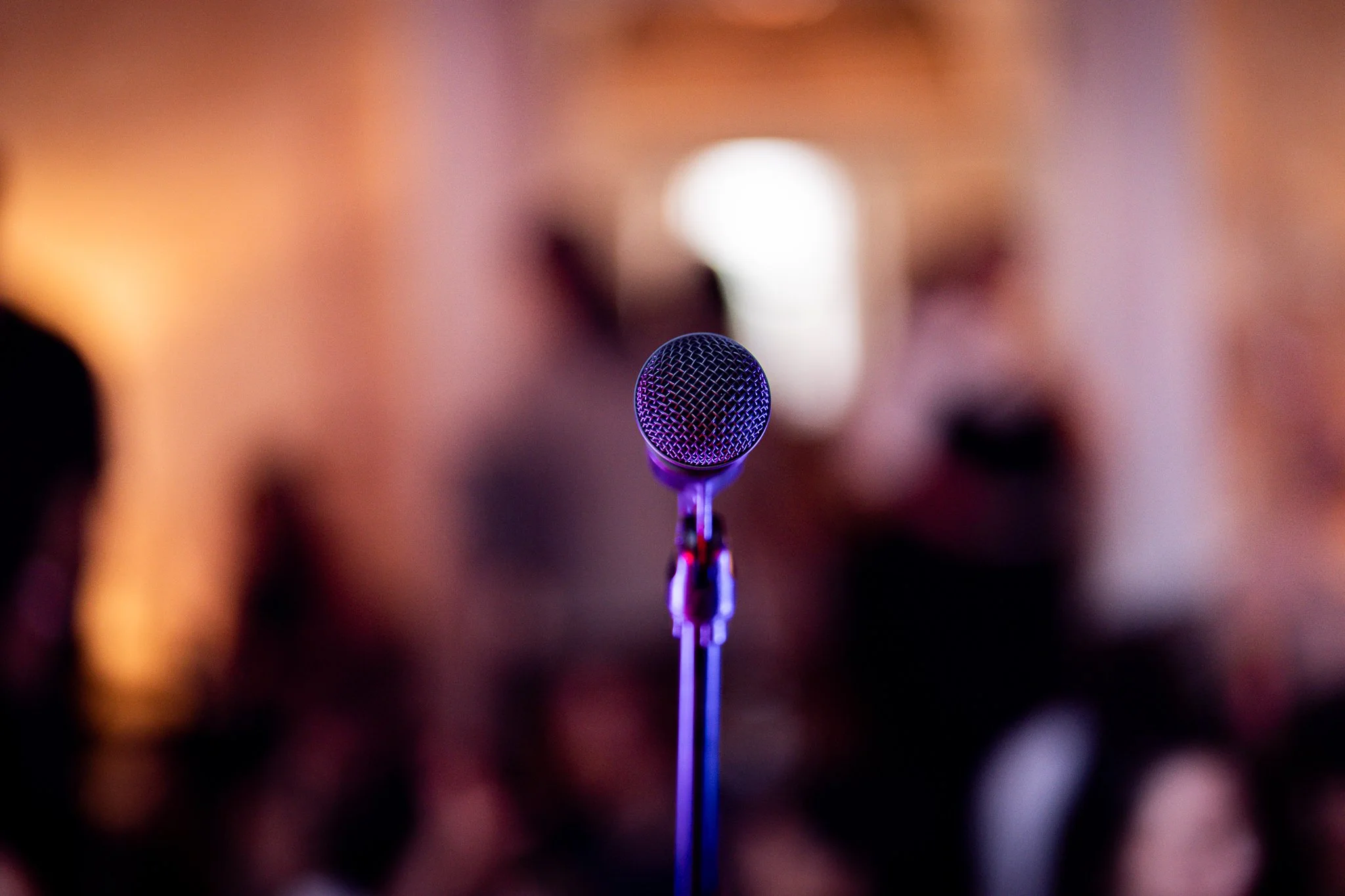 A microphone on a stand in focus against a blurred background with warm lighting at a What Does Not event.