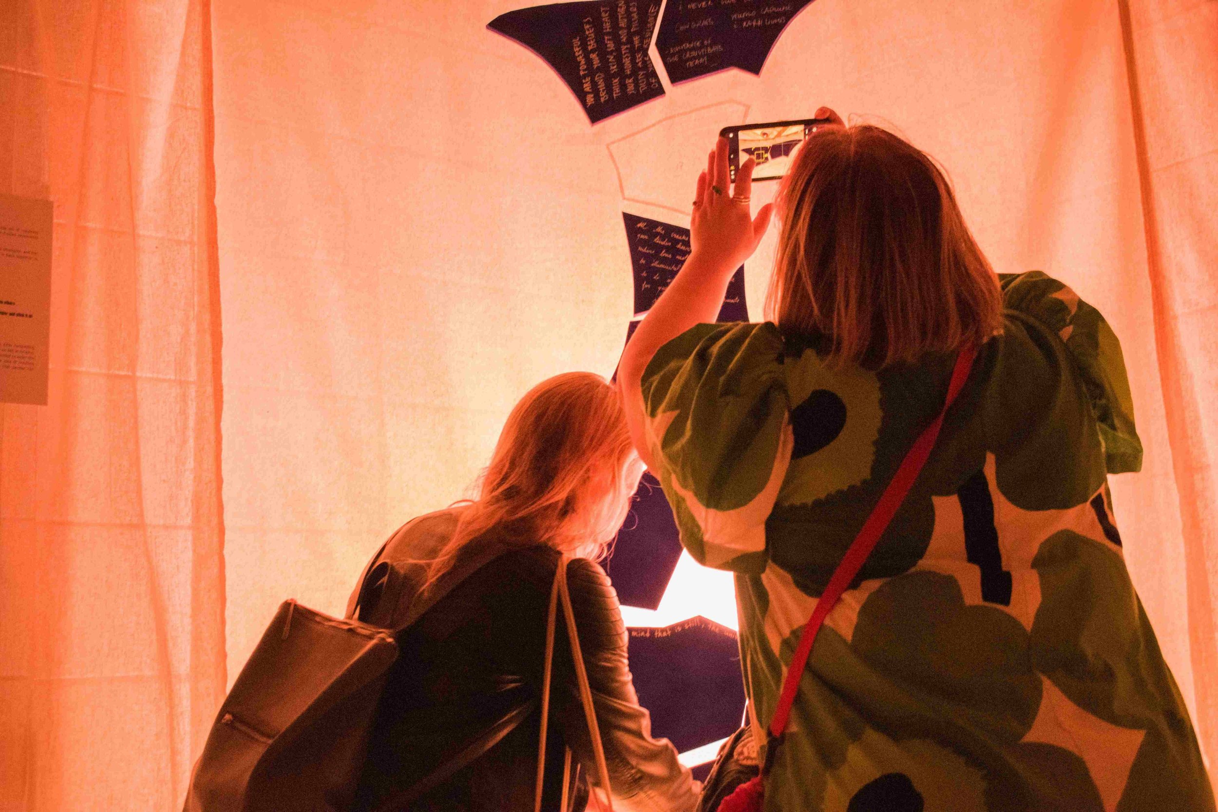 People at an exhibit or museum, with one person taking a photo of a display on the wall.