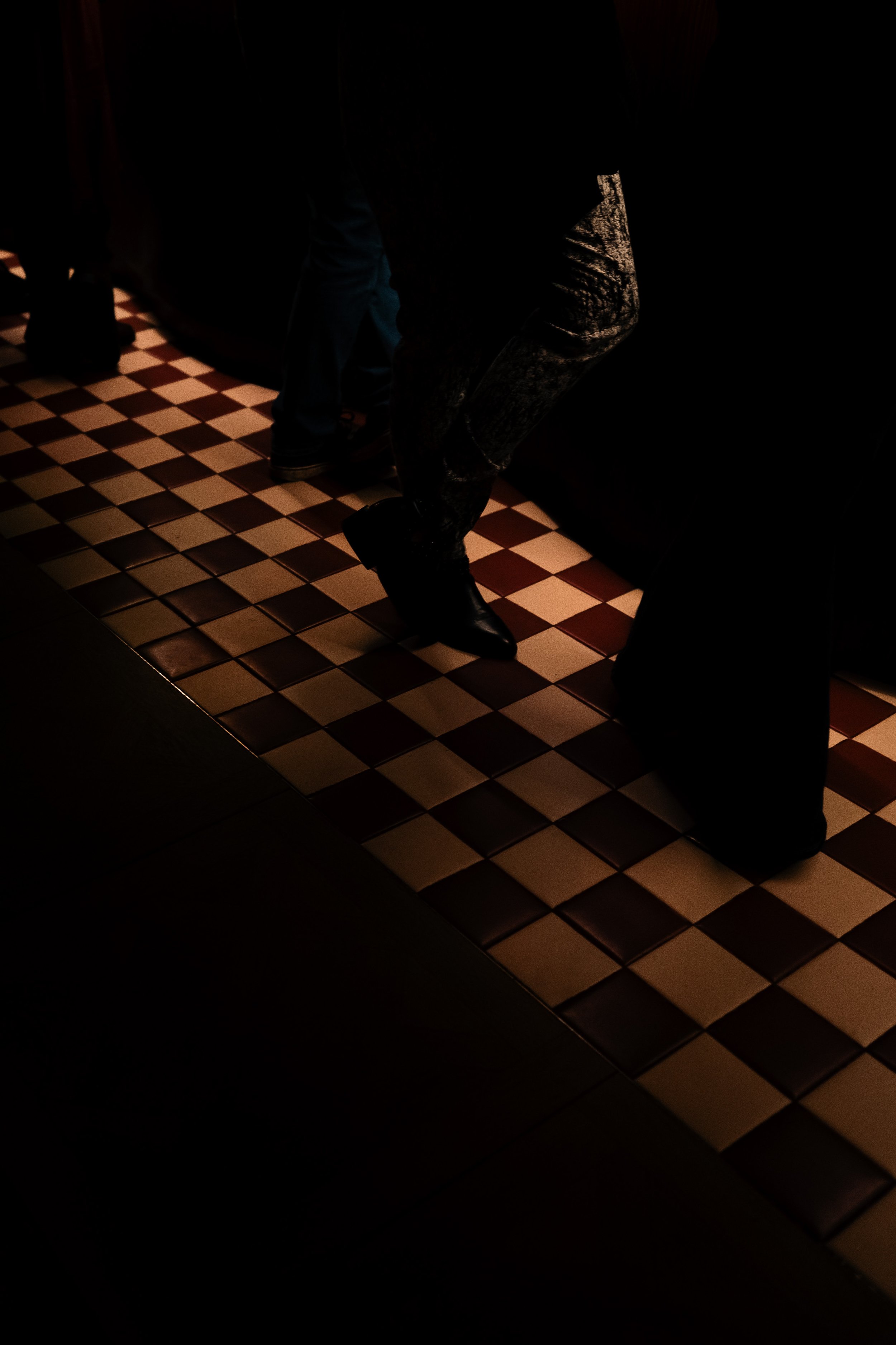 The feel of attendees at one of the What Does Not house parties, standing on a checkerboard tile floor, partially illuminated.