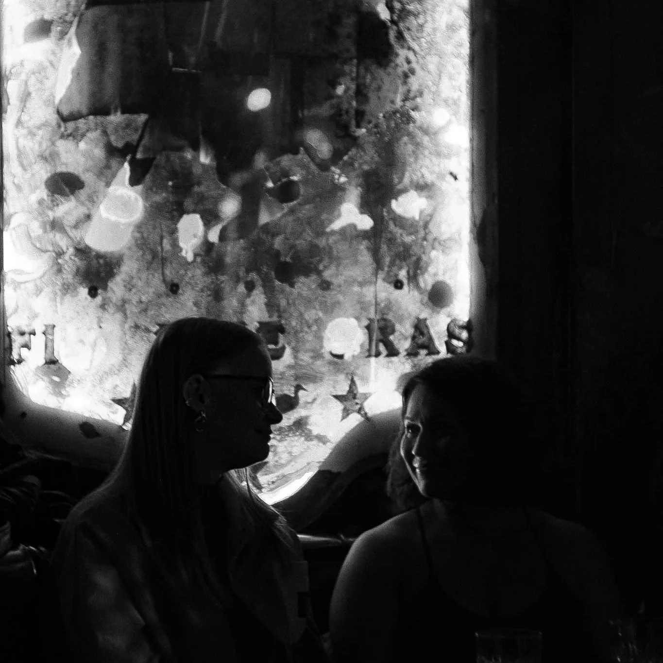 Two women chatting at a RAW uncensored storytelling night, sitting and talking below an illuminated panel