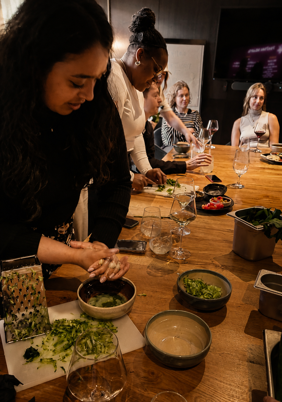 Women participating in a cooking class segment at a What Does Not culture club, chopping vegetables and preparing food, with wine glasses and bowls on the table, as part of learning a language in London
