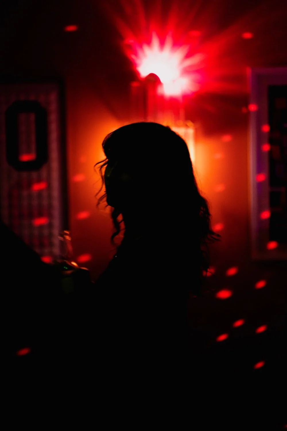 Silhouette of a woman with long hair at a What Does Not party with a disco light and laser effects creating red dots on the walls.