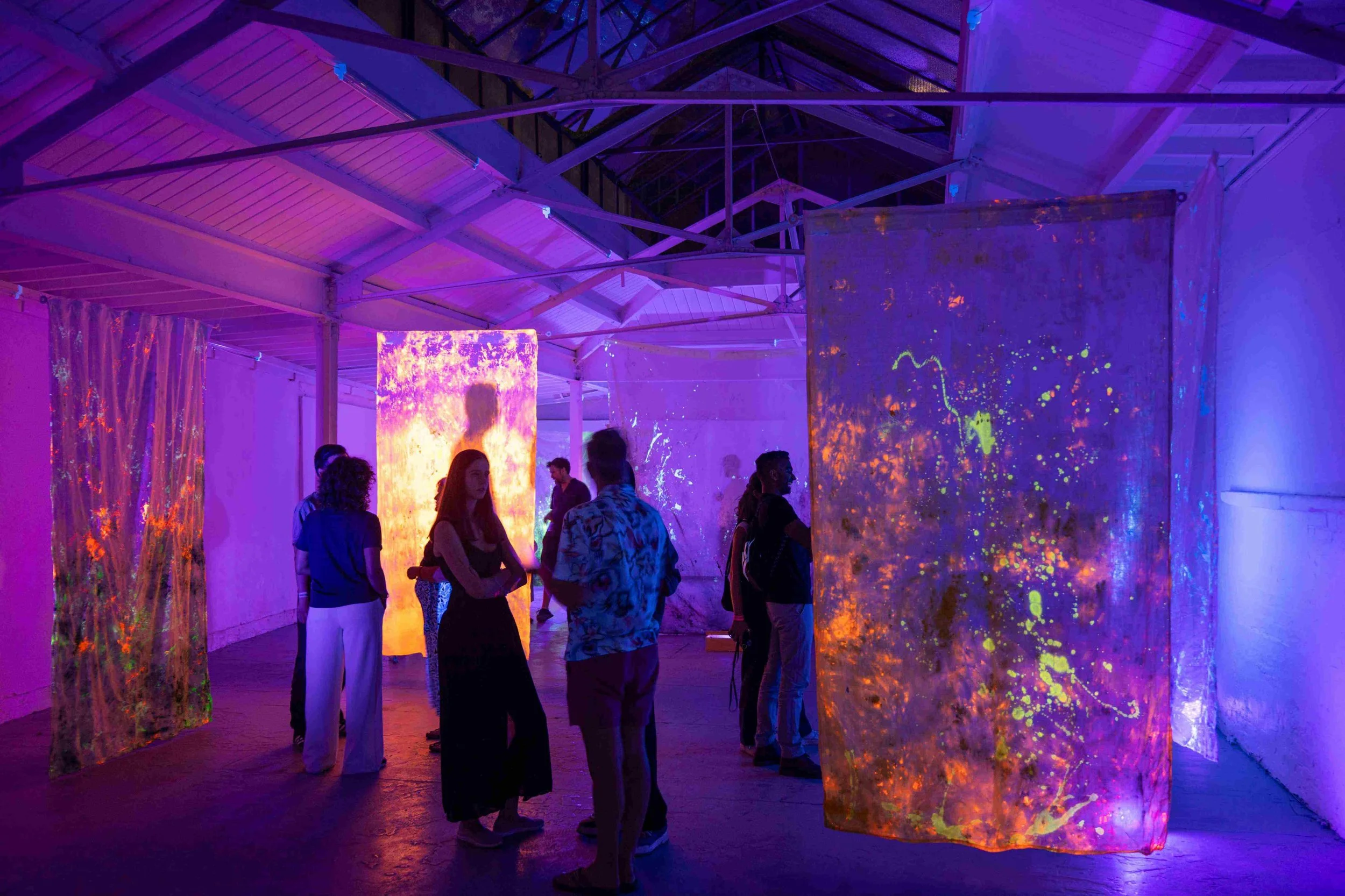 Art installation at RAW uncensored storytelling night, featuring UV lights and neon coloured sheets hanging in a large conservatory space