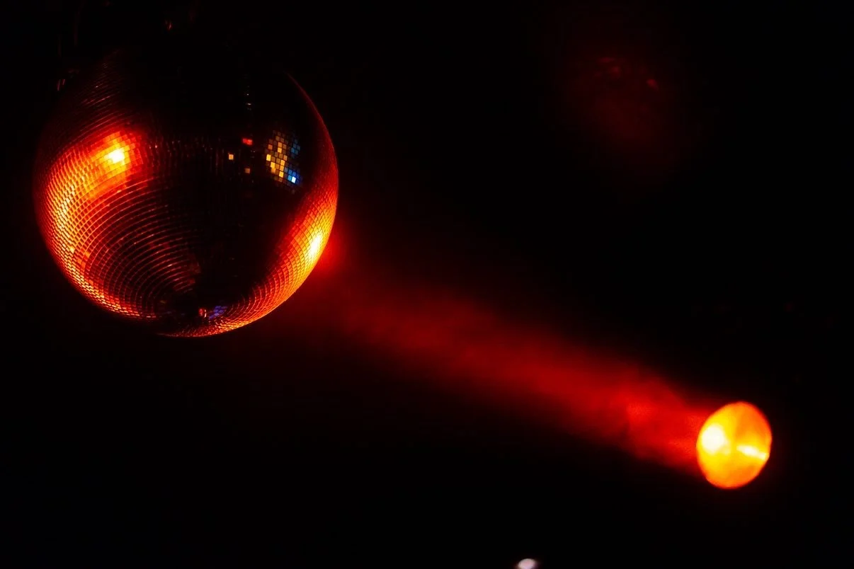 A mirror discoball reflecting red and orange lights with a red laser beam pointed from the right side at a What Does Not house party