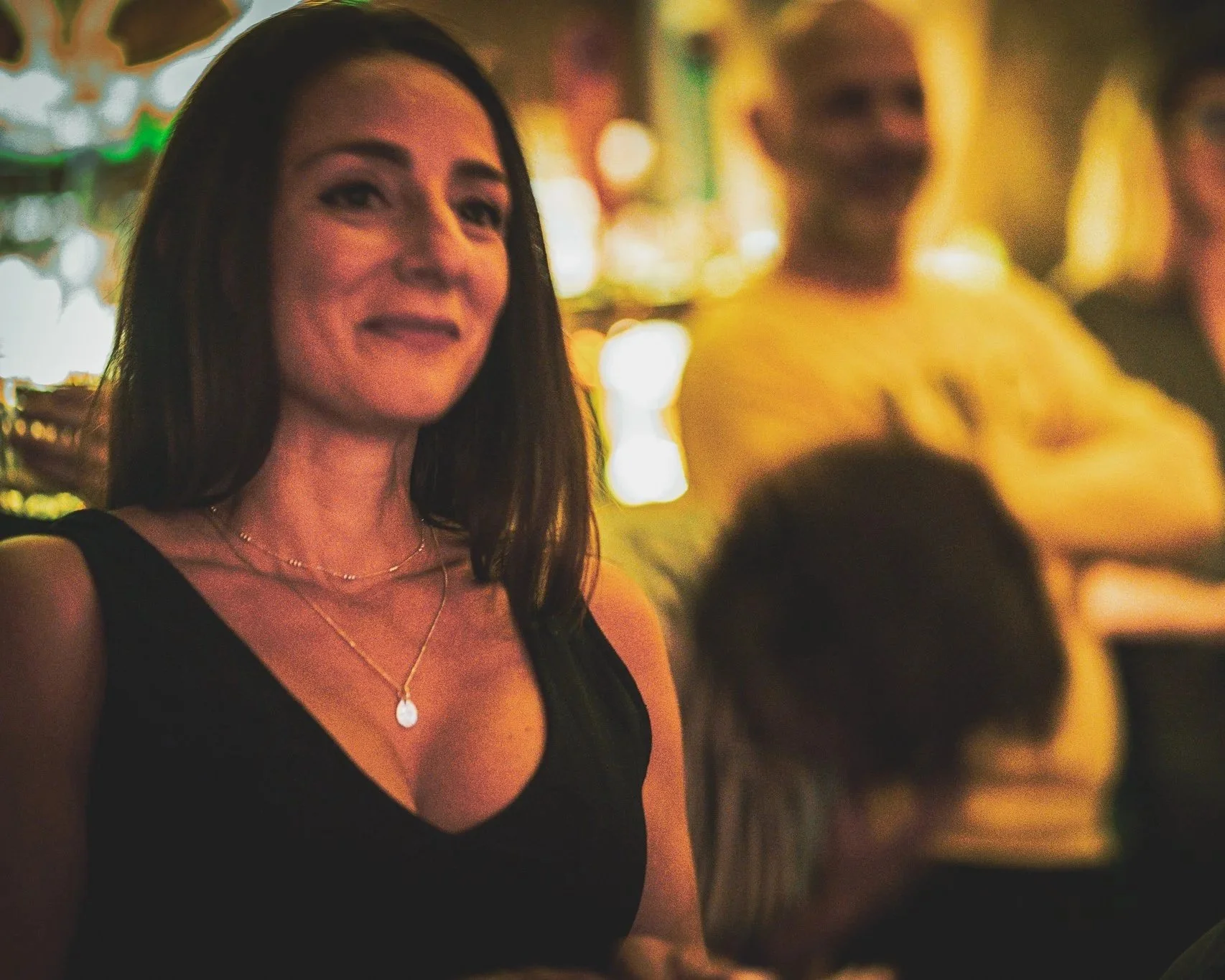 What Does Not head of people and projects, Tamara Mikaberidze, a woman smiling with a black top and a pendant necklace, in a dimly lit setting, likely at a social event or bar, with a blurred background featuring another woman and colorful lights.