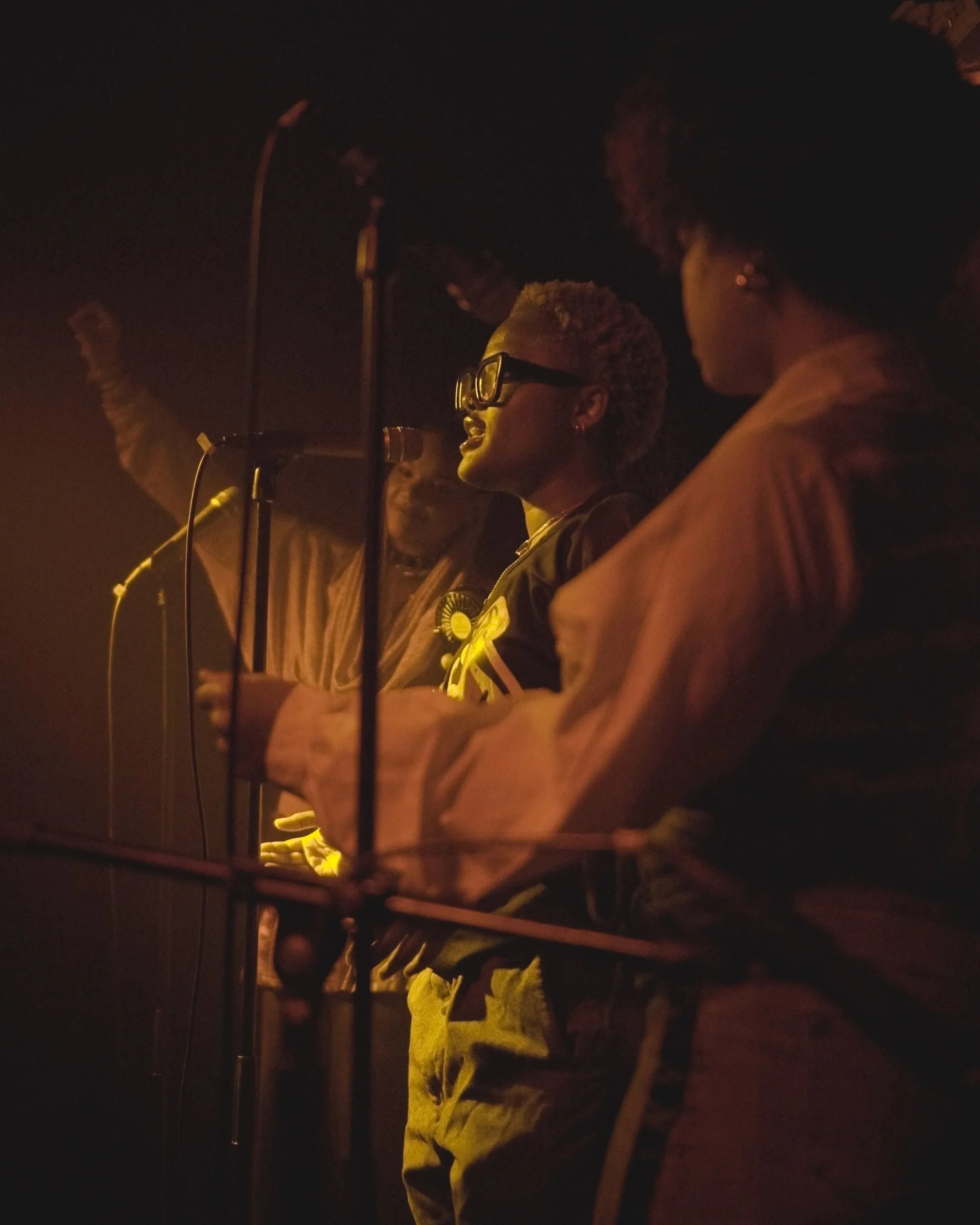 Emerging musicians perform and vocalists sing, with warm lighting illuminating their faces, at a What Does Not live music night
