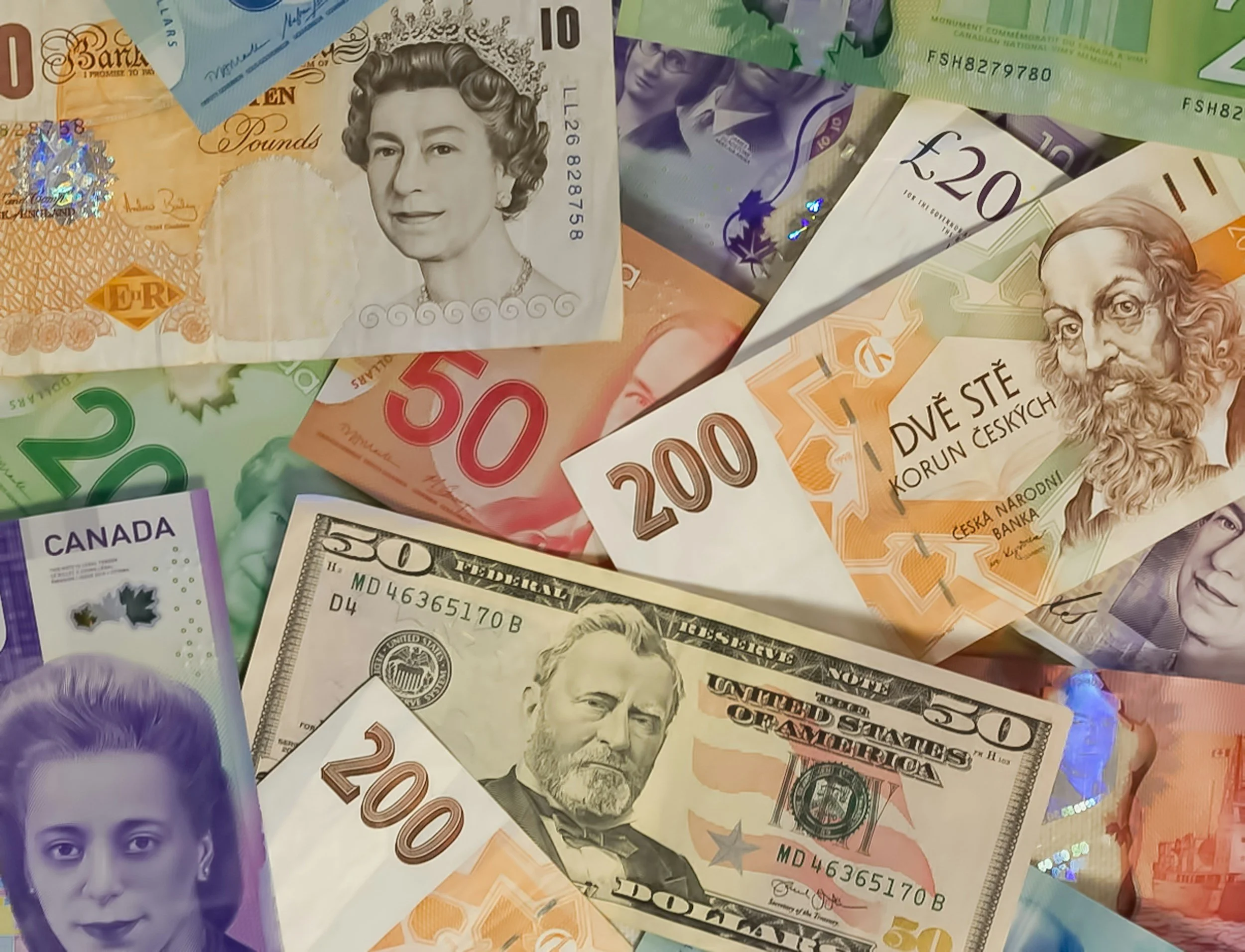 A variety of paper currency bills from different countries, including UK pounds, US dollars, and Canadian dollars, arranged in overlapping layers.