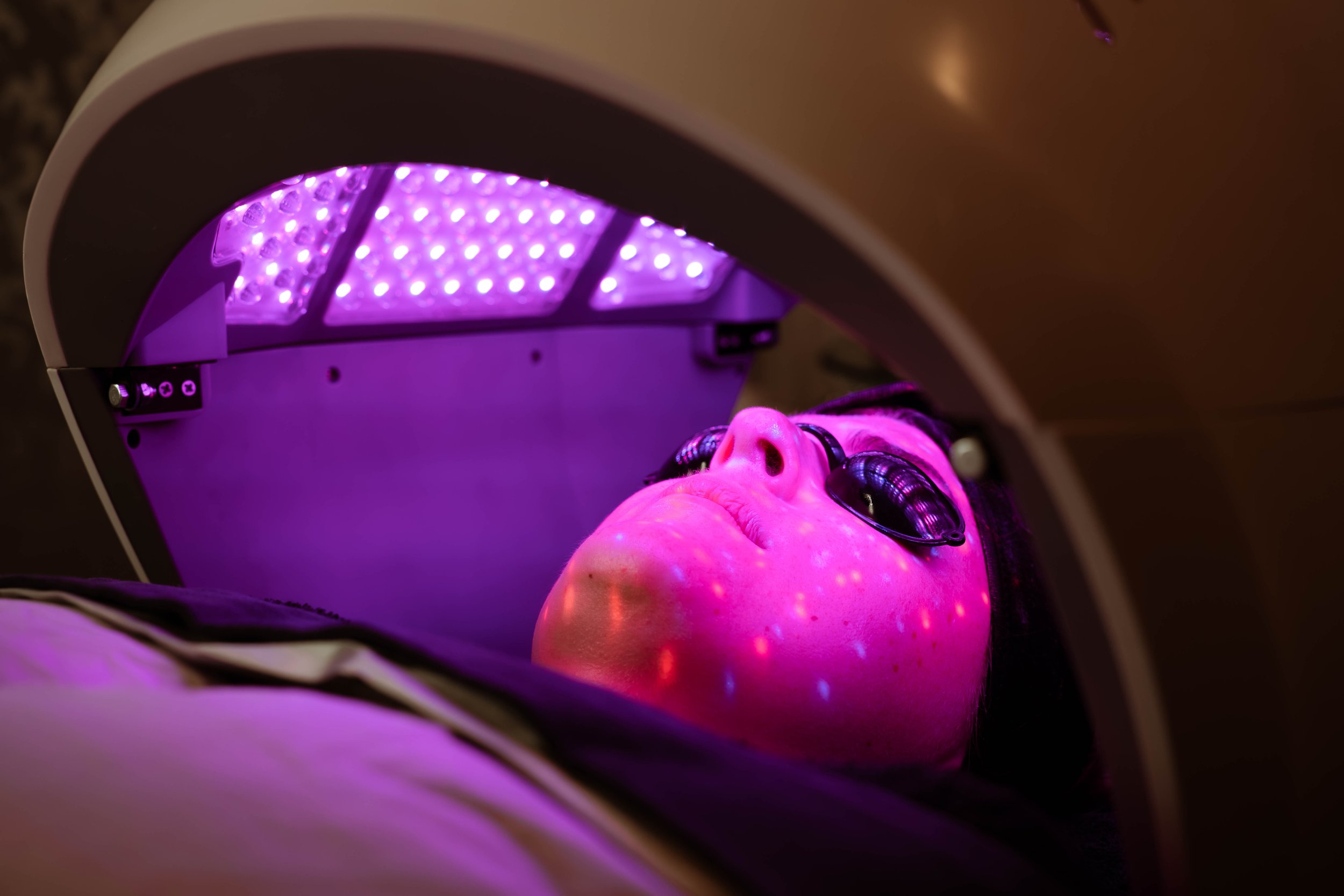 Person lying under a purple LED light as part of a skin or beauty treatment at Cut Above Salon in Hastings, Hawke's Bay