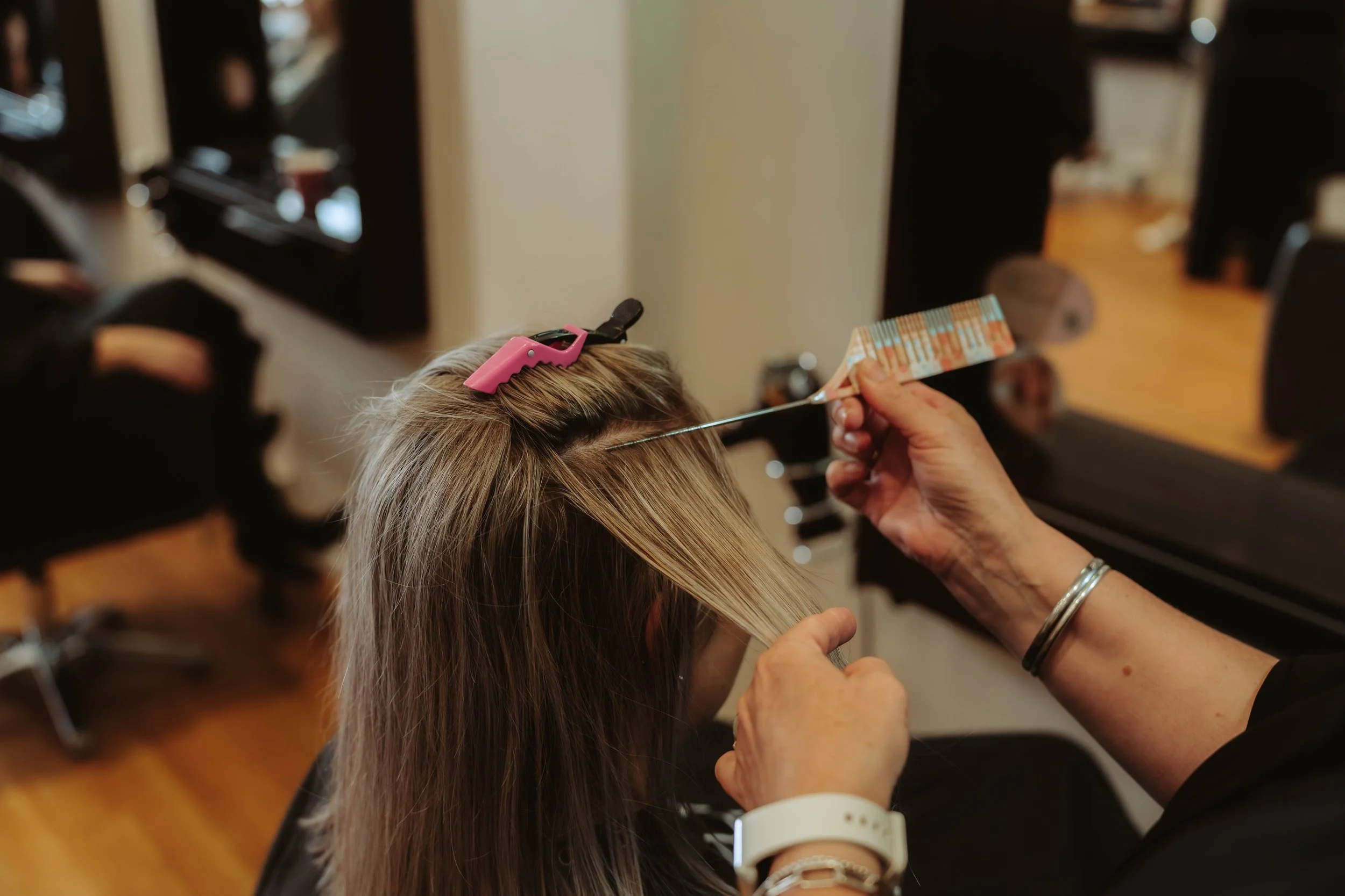 A hairdresser using a metal end comb to section the hair for foils on the blonde clients hair