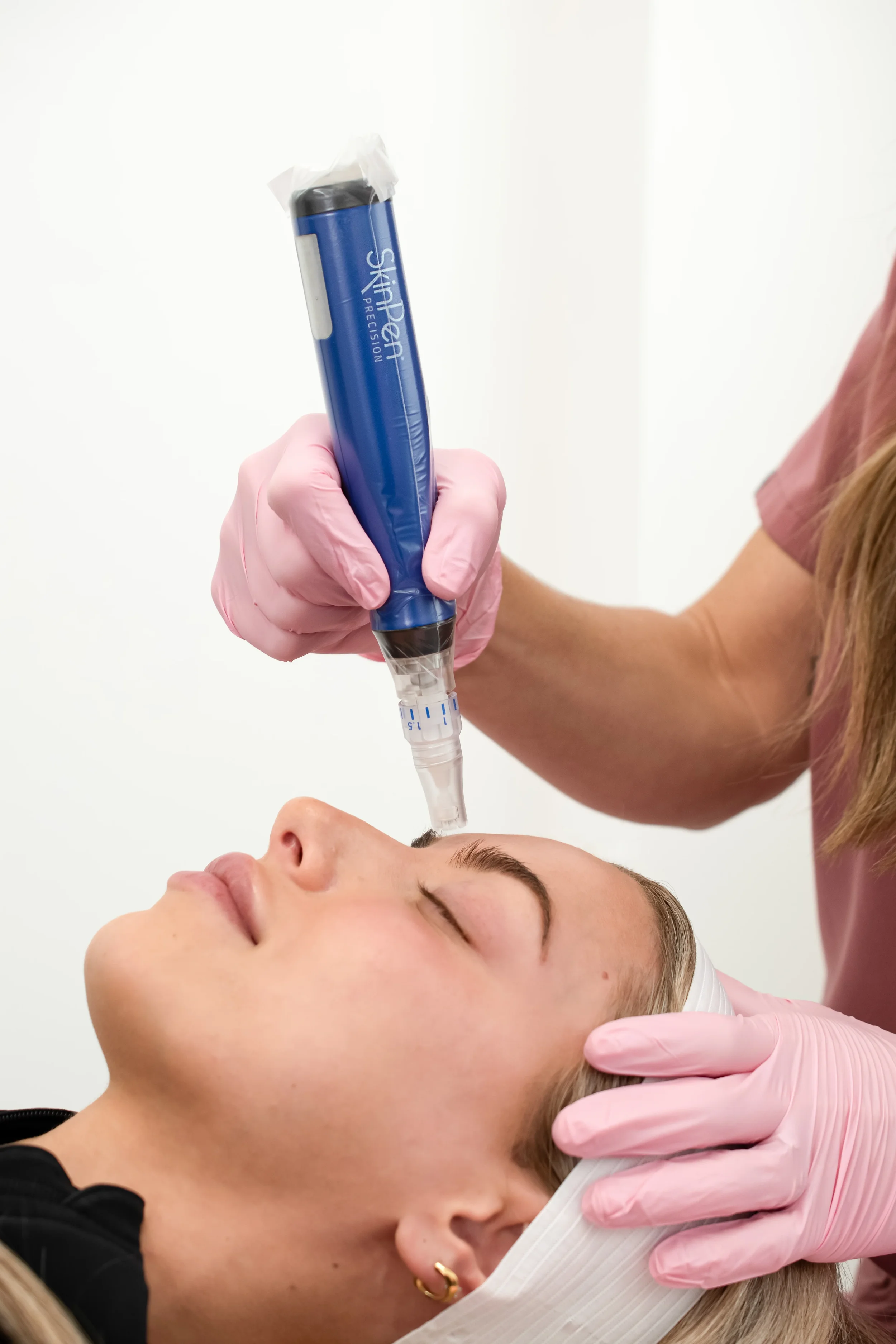 A person receiving a cosmetic injection in their face, lying down with eyes closed, with a healthcare professional wearing pink gloves administering the treatment.