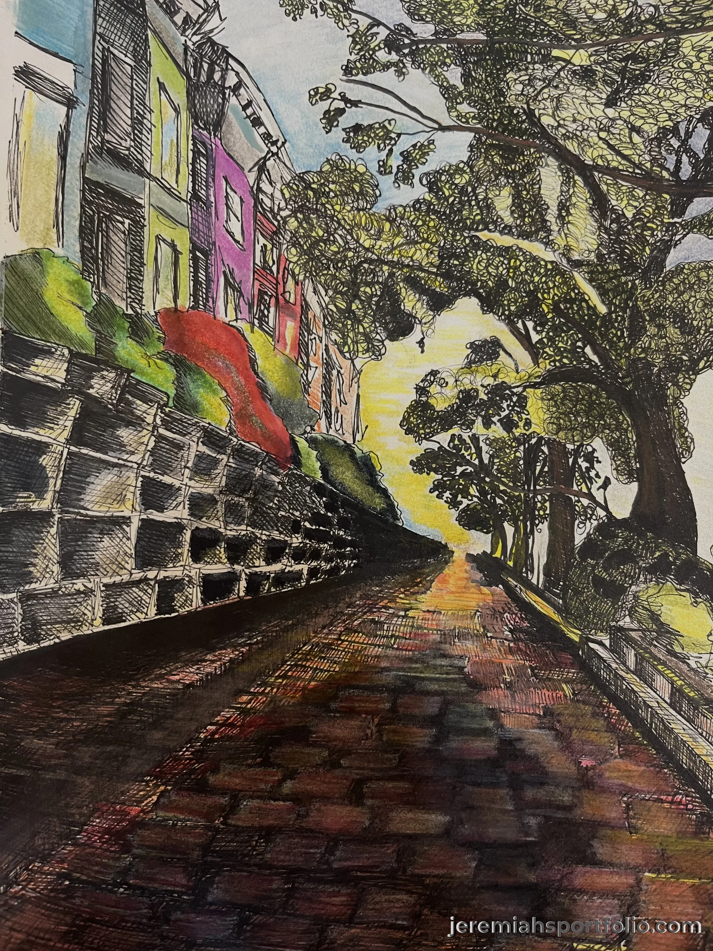 A street scene with a stone retaining wall on the left, colorful buildings with windows and balconies, tall trees with lush green leaves on the right, and a pink and yellow sunset sky in the background.