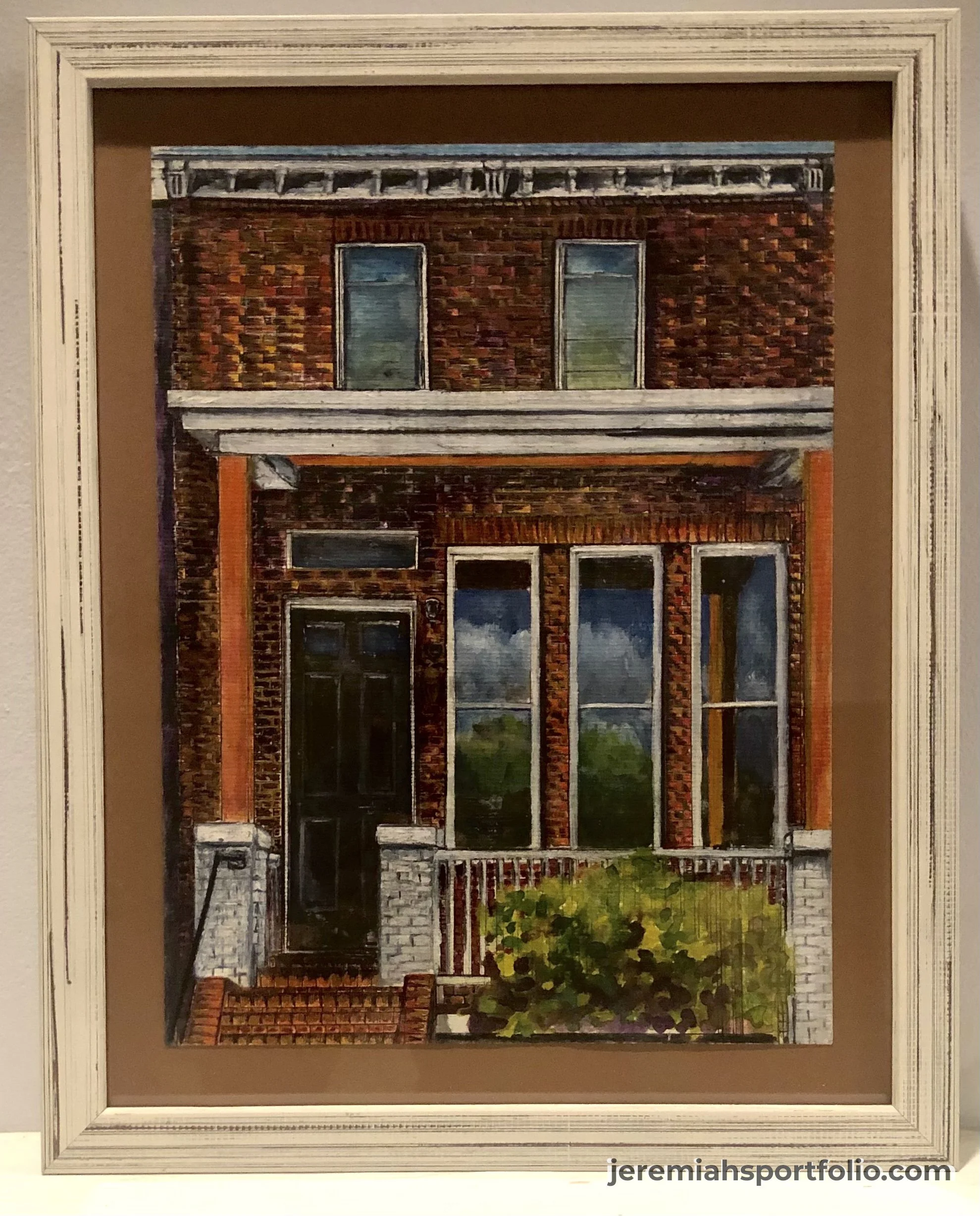 Painting of a brick building with windows, a door, and a small garden in front, framed in a white decorative frame.