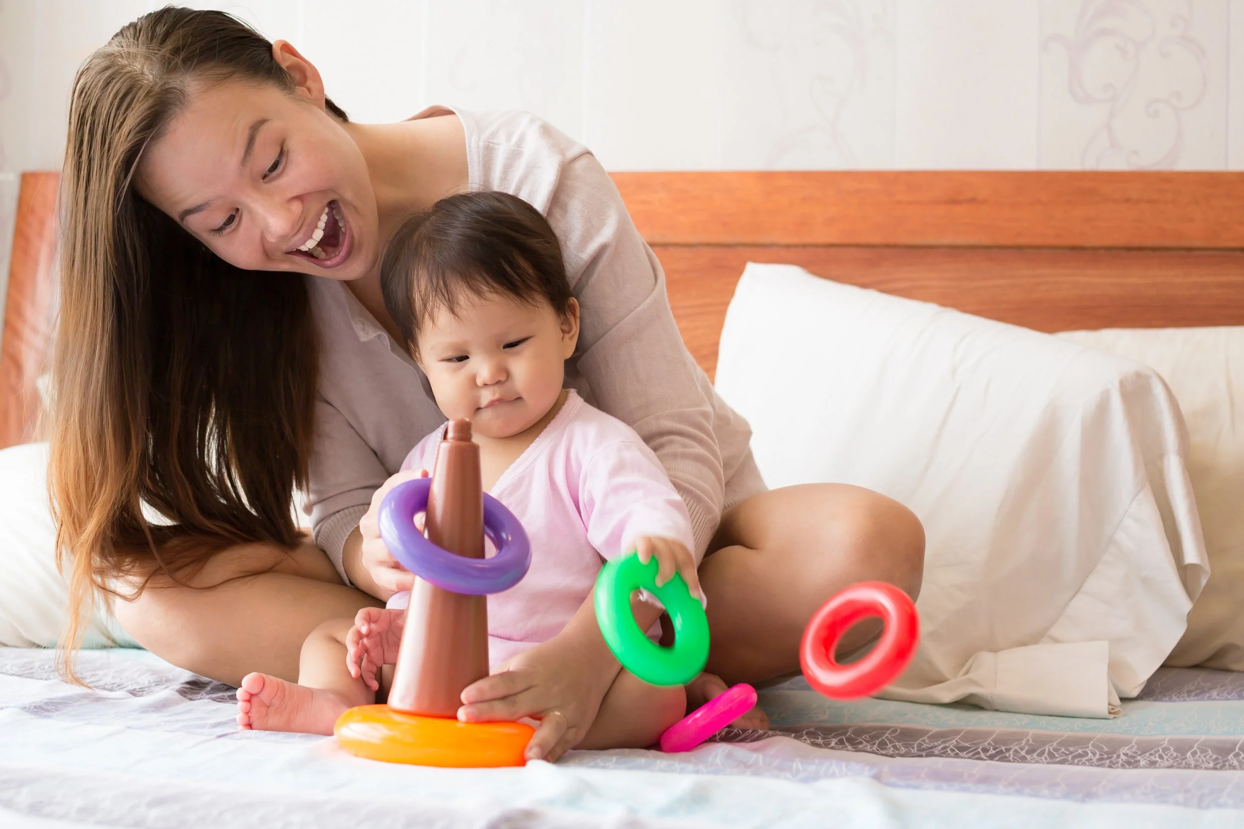 mom and child playing with ring toy on bed