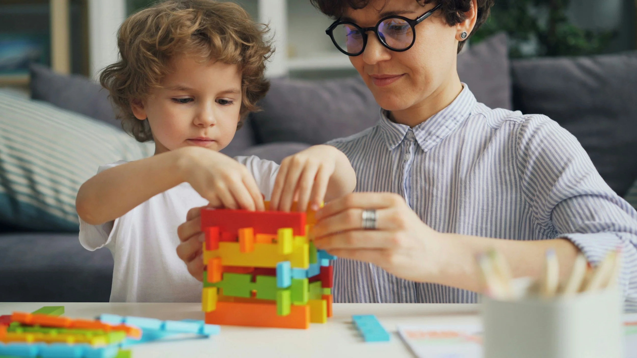 Woman with glasses helping young boy build blocks