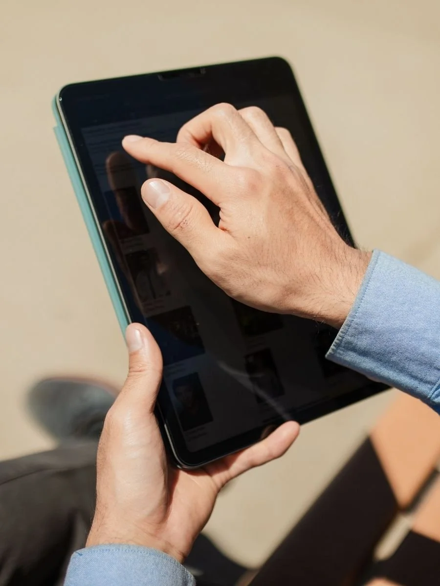A person holding a tablet and using their other hand to tap the screen.