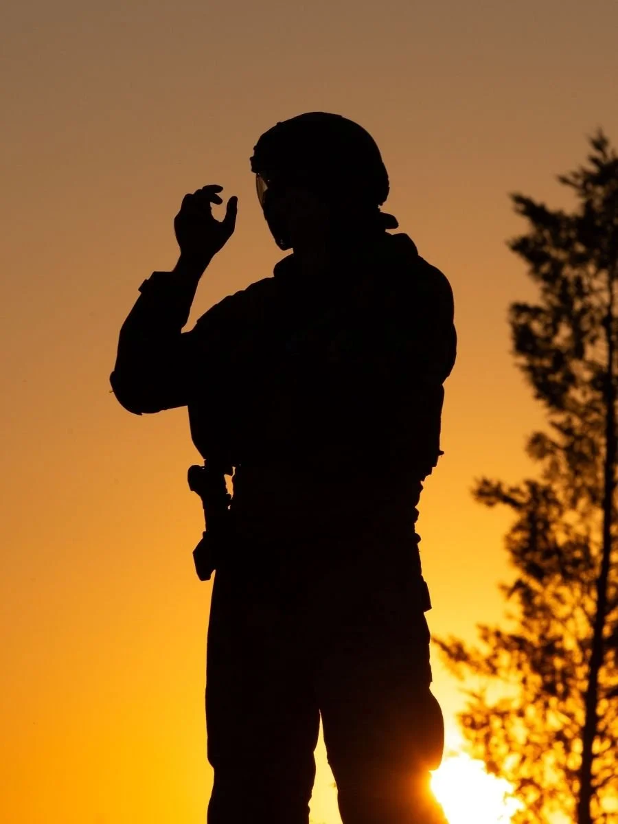 Silhouette of a person adjusting goggles at sunset outdoors, with trees in the background.