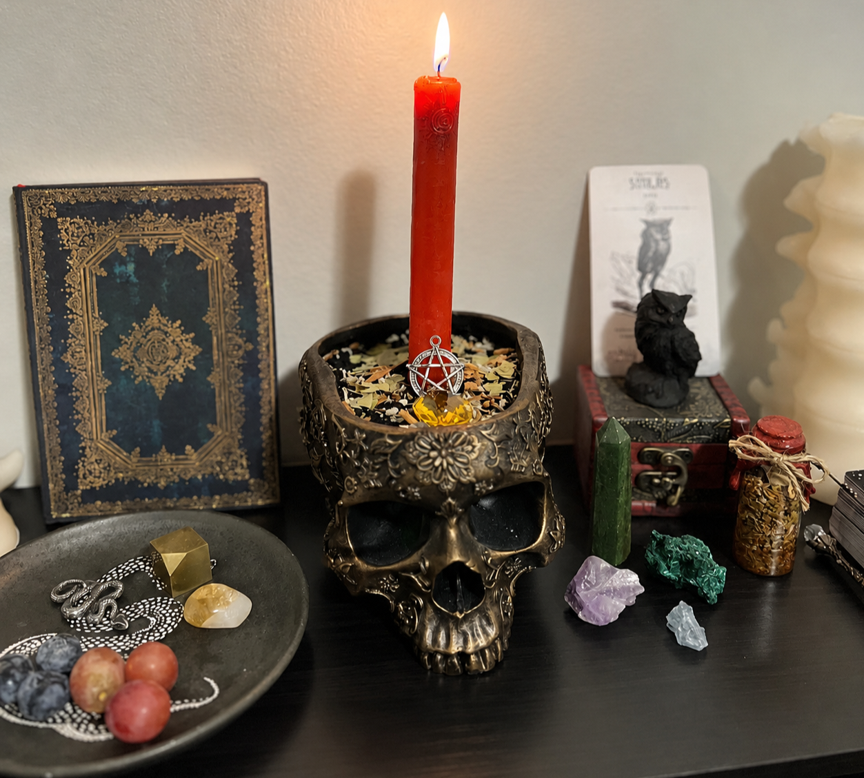Decorative altar with a red candle on a skull-shaped holder, surrounded by crystals, jewelry, and small boxes, with occult and spiritual items.