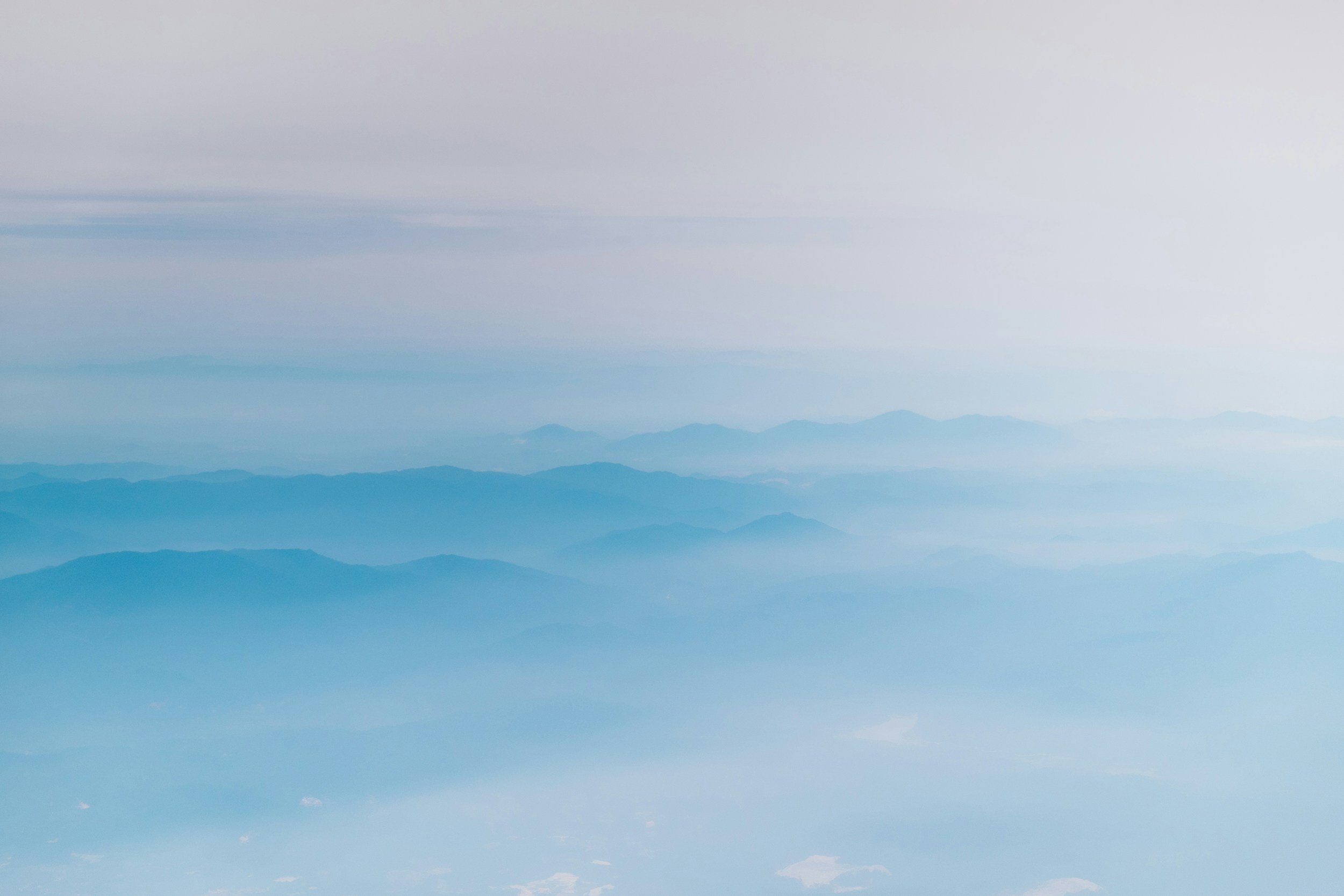 A scenic view of multiple mountain ranges with layers of mist and clouds, creating a serene and expansive landscape.