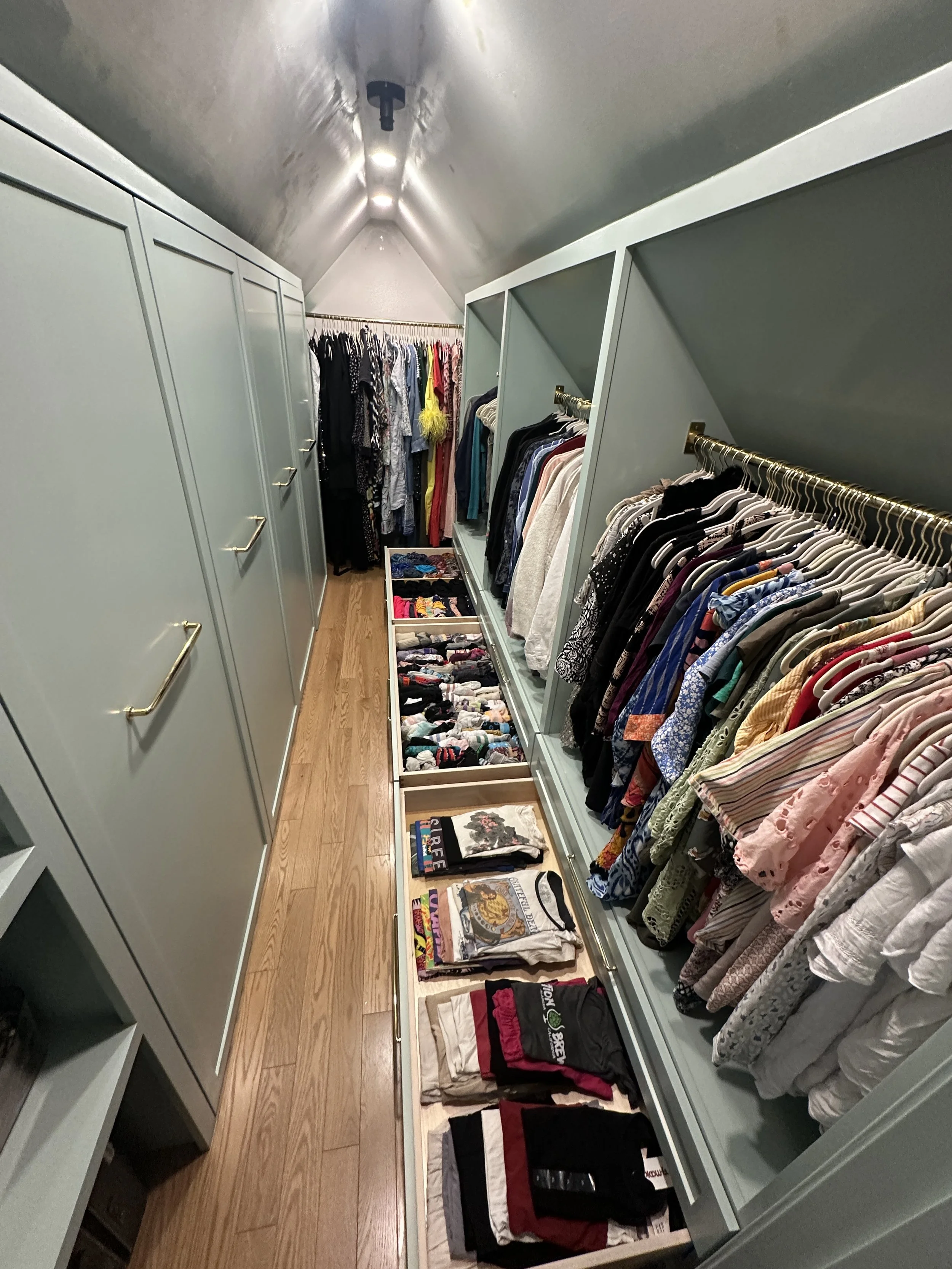 A walk-in closet with built-in cabinets, hanging clothes, folded clothes, and storage boxes.