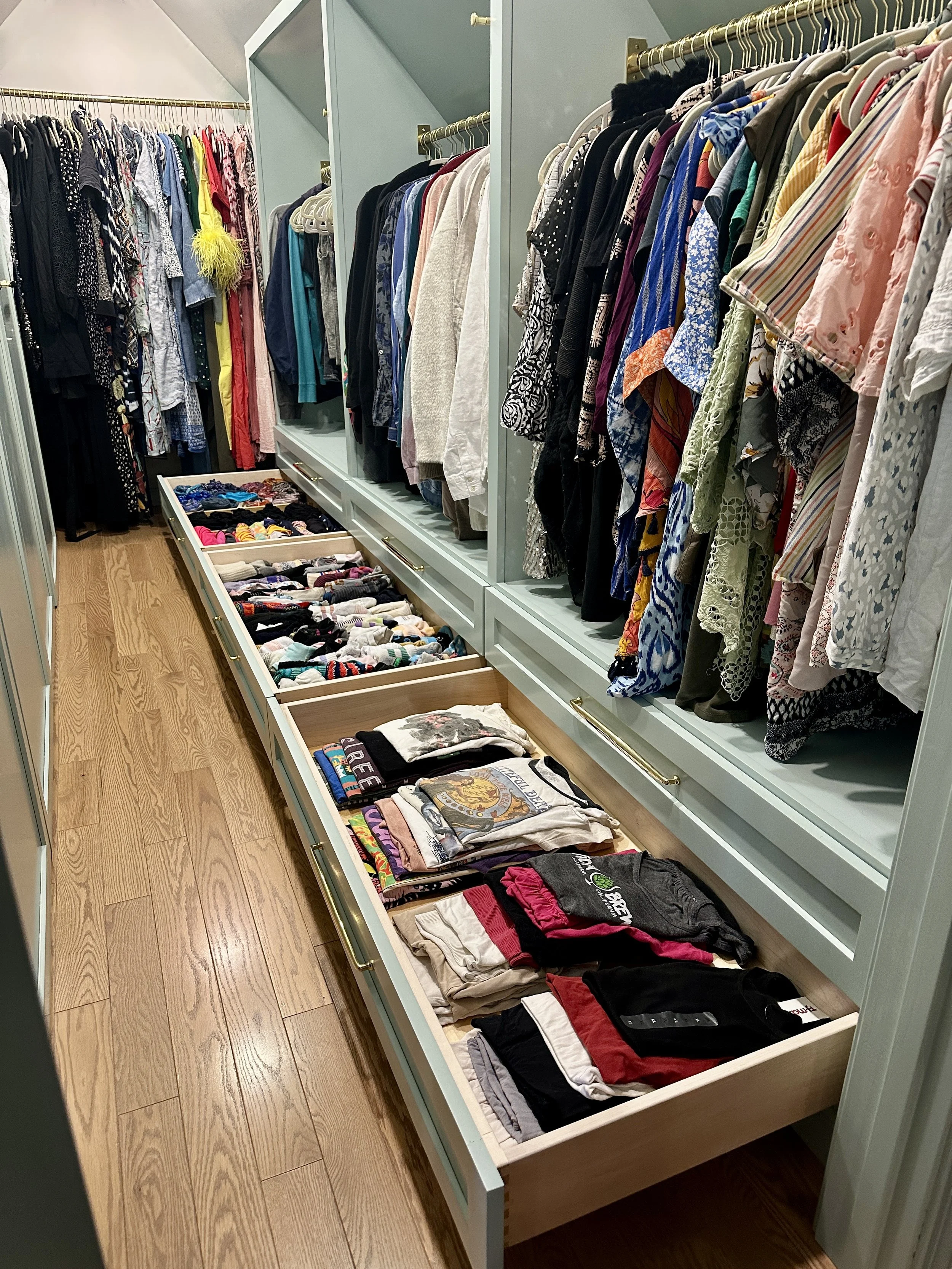 A closet with hanging clothes and open drawers filled with folded t-shirts and socks.