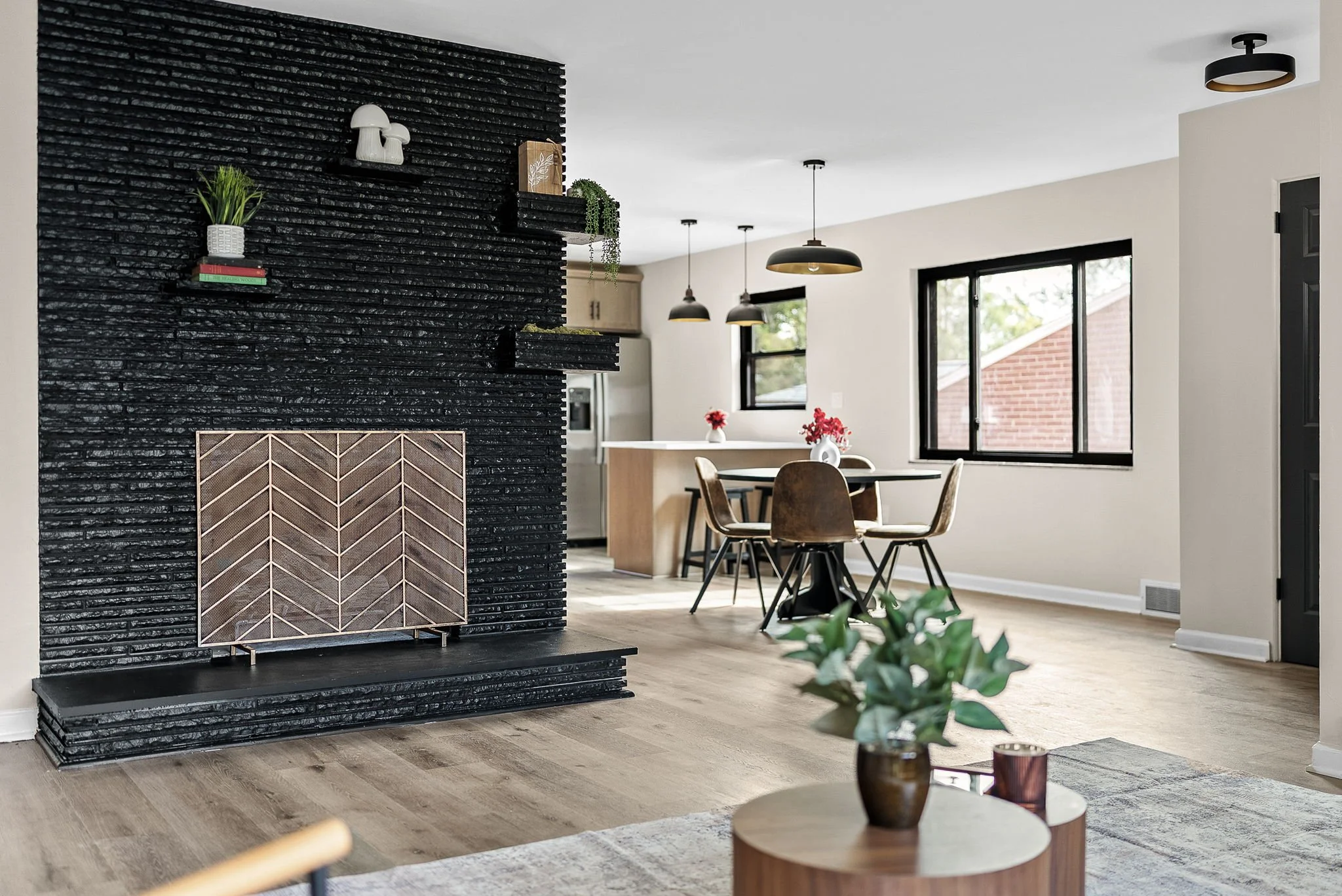 Interior of a modern living room with a black textured fireplace, a round dining table with four chairs, black pendant lights, large windows, and decorative items like plants and vases representing the home buying journey in Greater Pittsburgh.