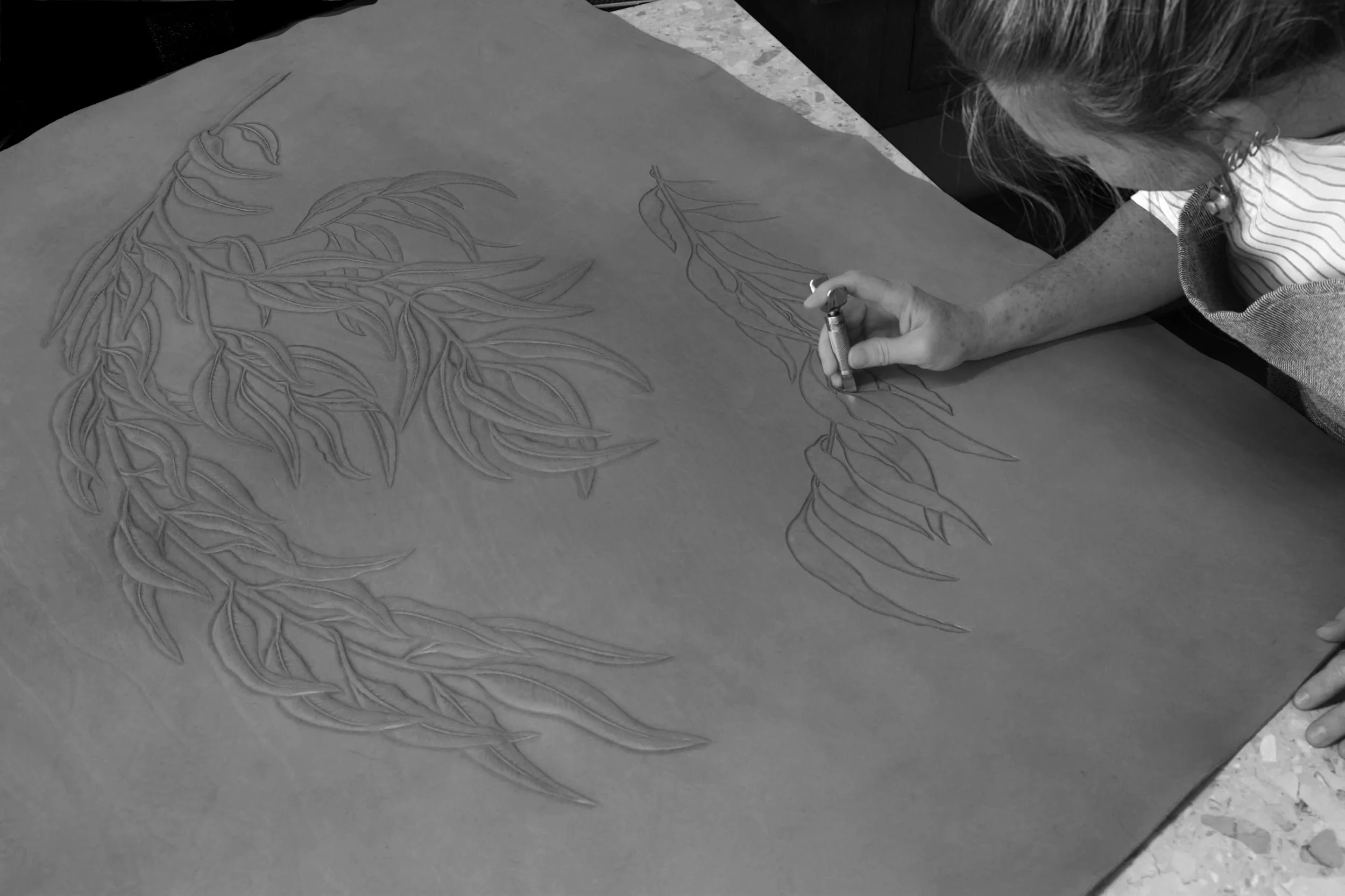 Adrienne carving decorative leaves on leather.
