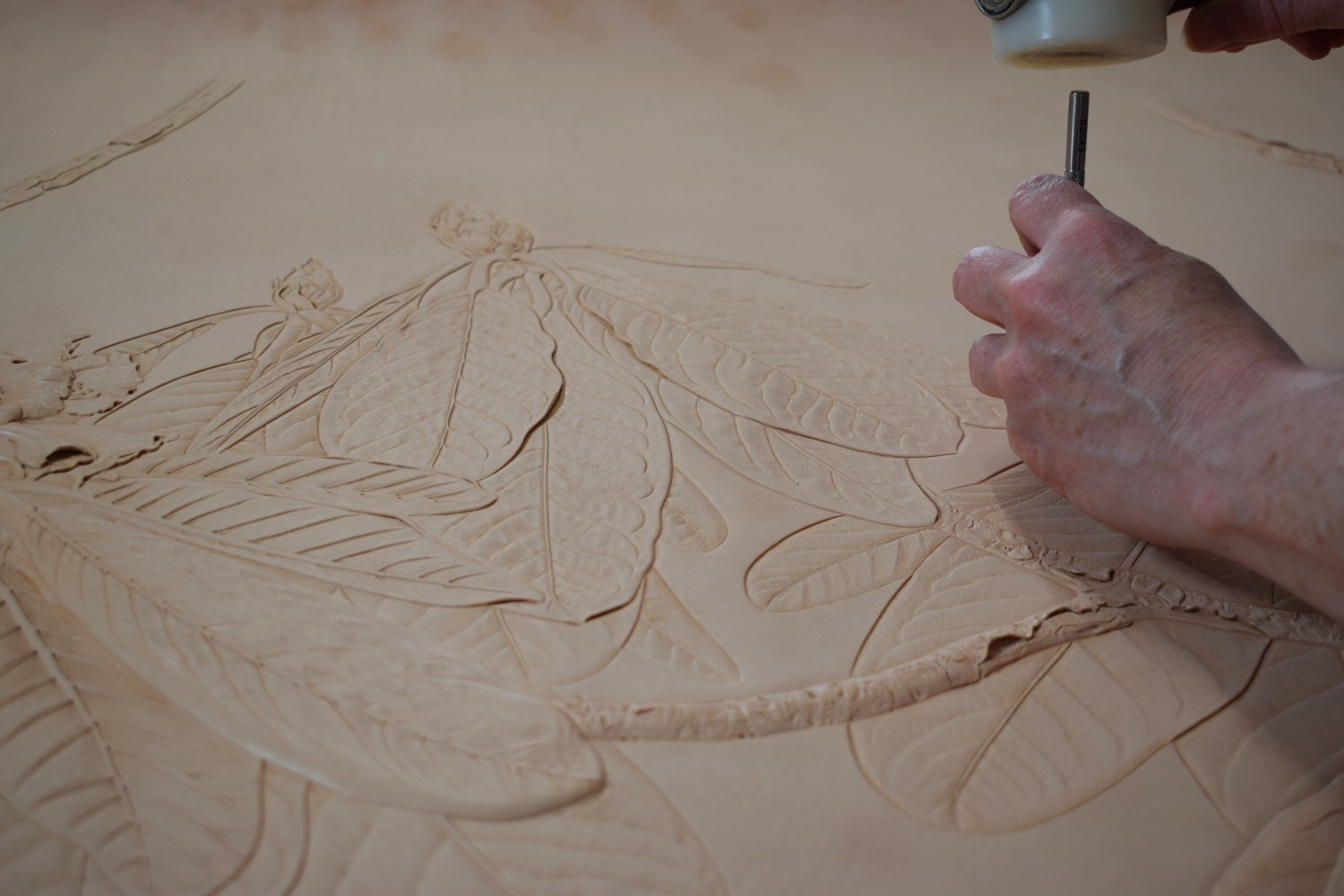 Adrienne carving botanical details of Rhododendron falconeri on natural leather.