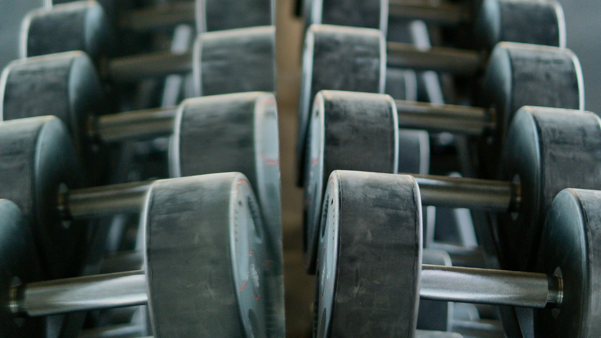Stacked dumbbells with dark handles and black rubber-coated weights in a gym or fitness center.
