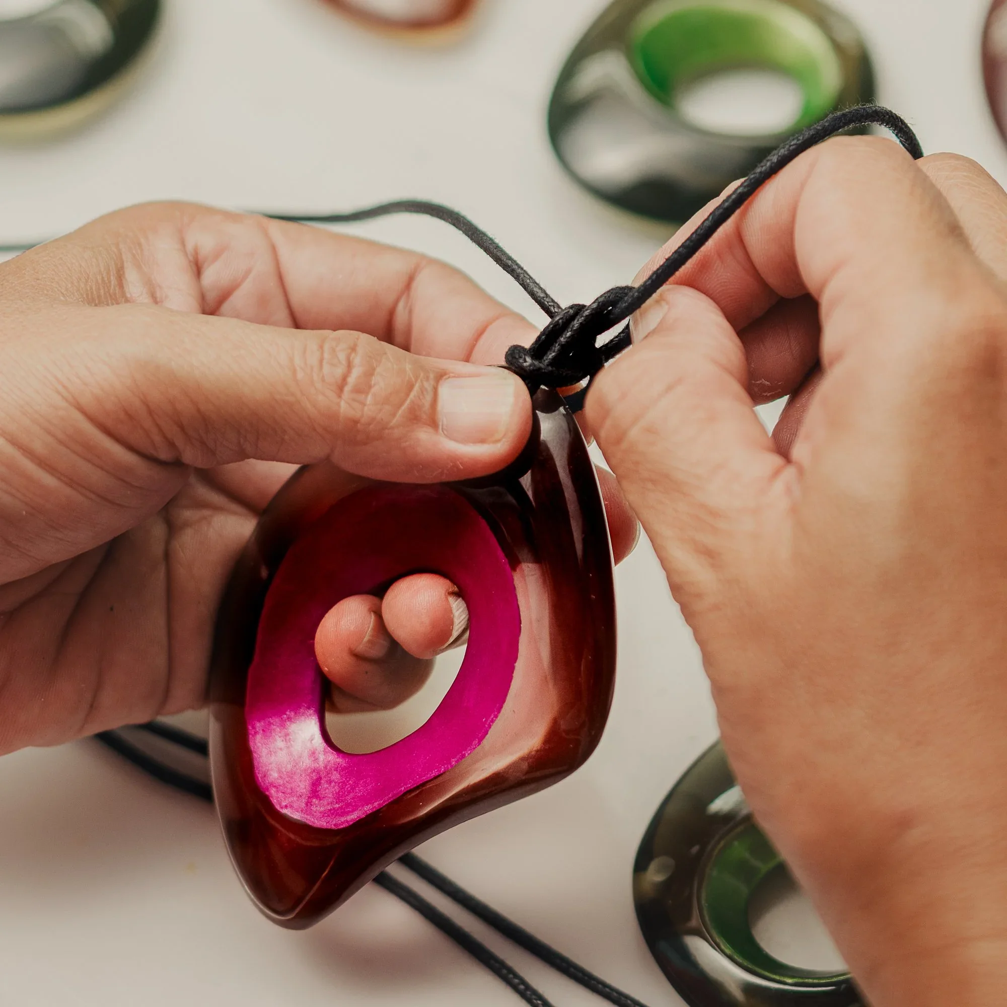 Close-up of hands stringing colourful ZSISKA resin beads by hand