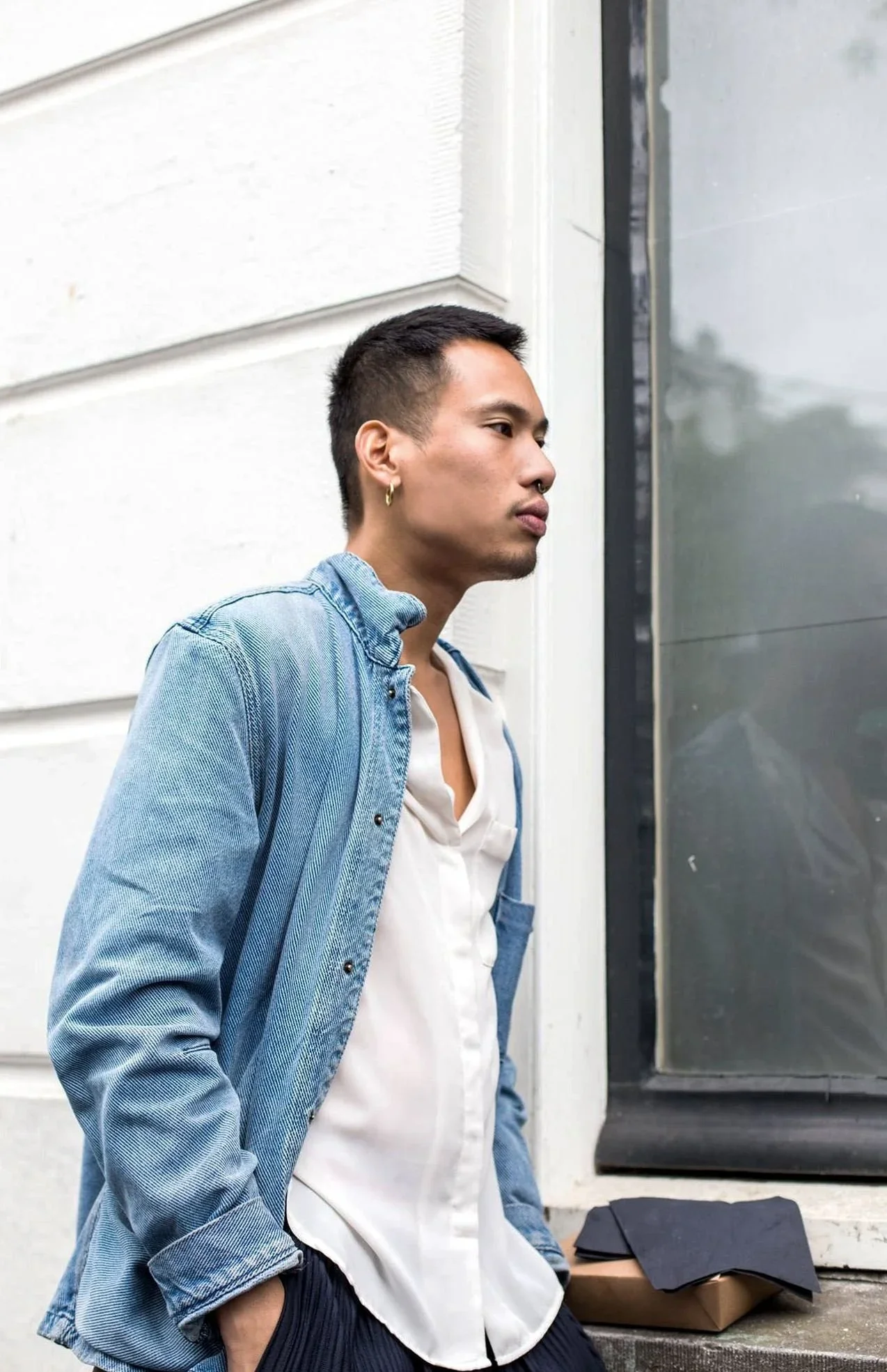 Jonathan Ho wearing a denim jacket standing against a white paneled wall