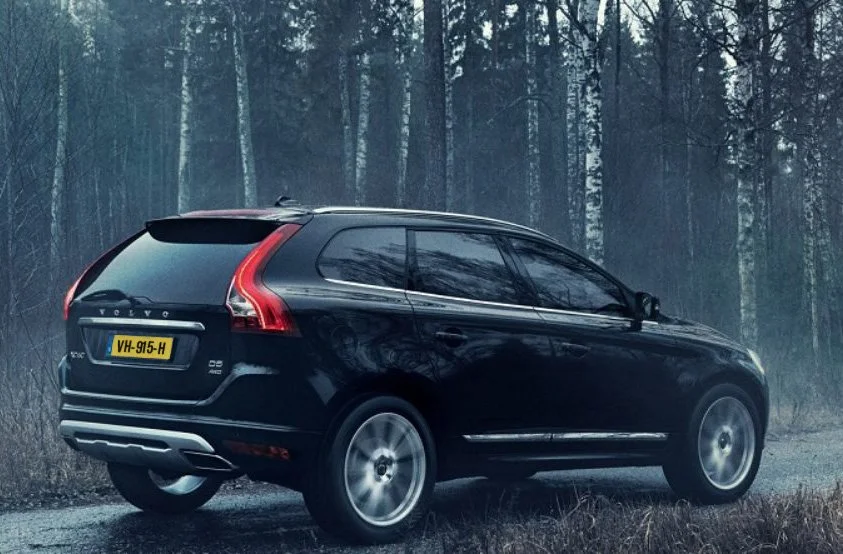Black Volvo SUV parked on the side of a forest road in a wooded area with bare trees and a foggy atmosphere.