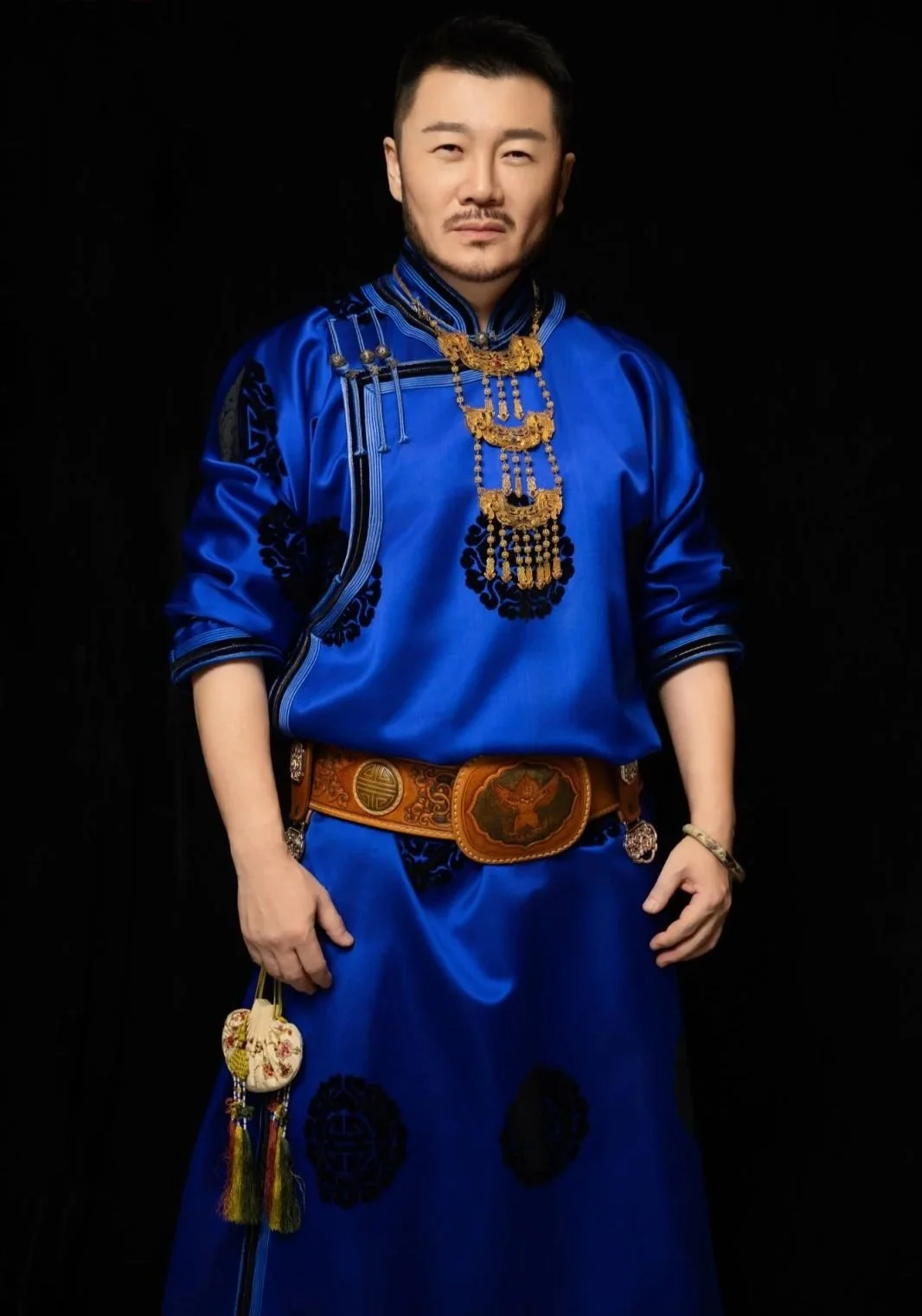 Portrait of fashion designer Hu Sheguang wearing a blue traditional Mongolian garment