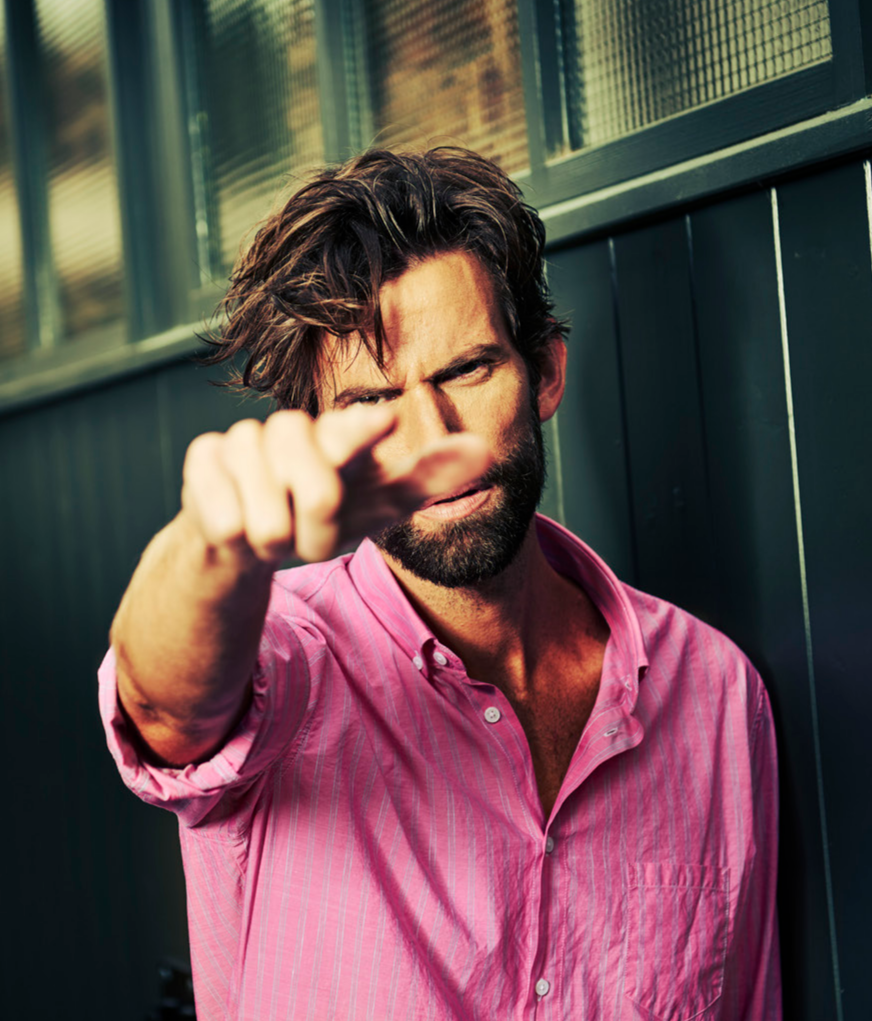 Man in pink shirt pointing at camera in front of window blinds, representing the Signum brand