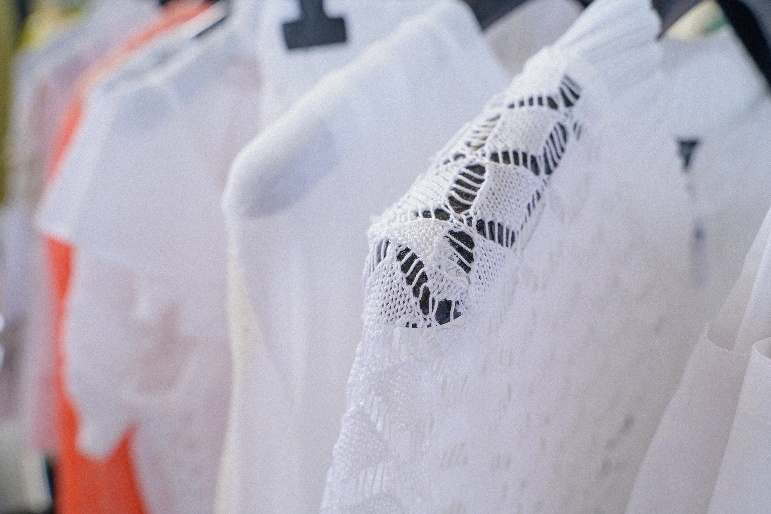 Close-up of white crochet-lace knitwear garments hanging on a clothing rack
