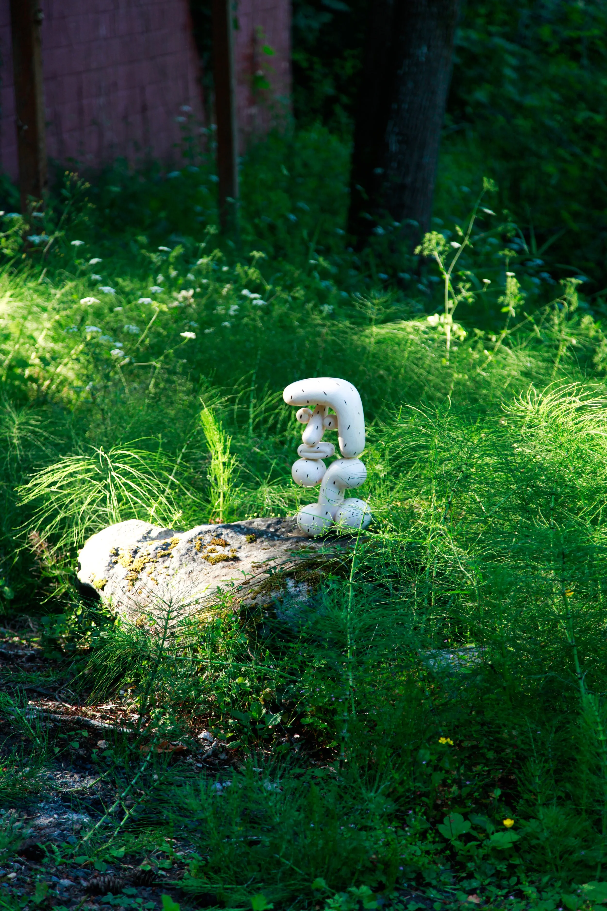 A small sculpture of a snake on a rock in a lush green garden with grass and plants.