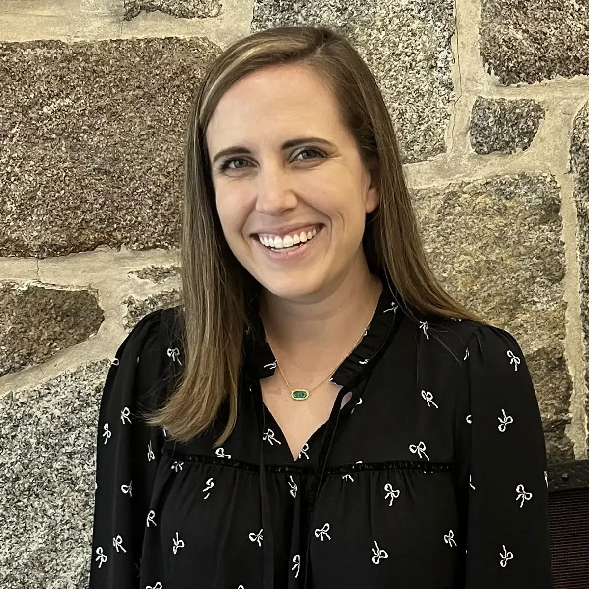 Danielle Tobin, smiling, wearing a black shirt, standing in front of a stone wall. Therapist at Edith Schatz LLC