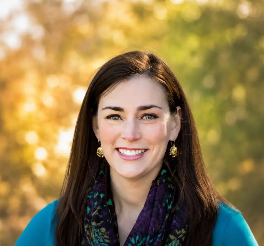 Edie Schatz smiling outdoors with a blurred background of trees and sunlight. Therapist and owner at Edith Schatz LLC