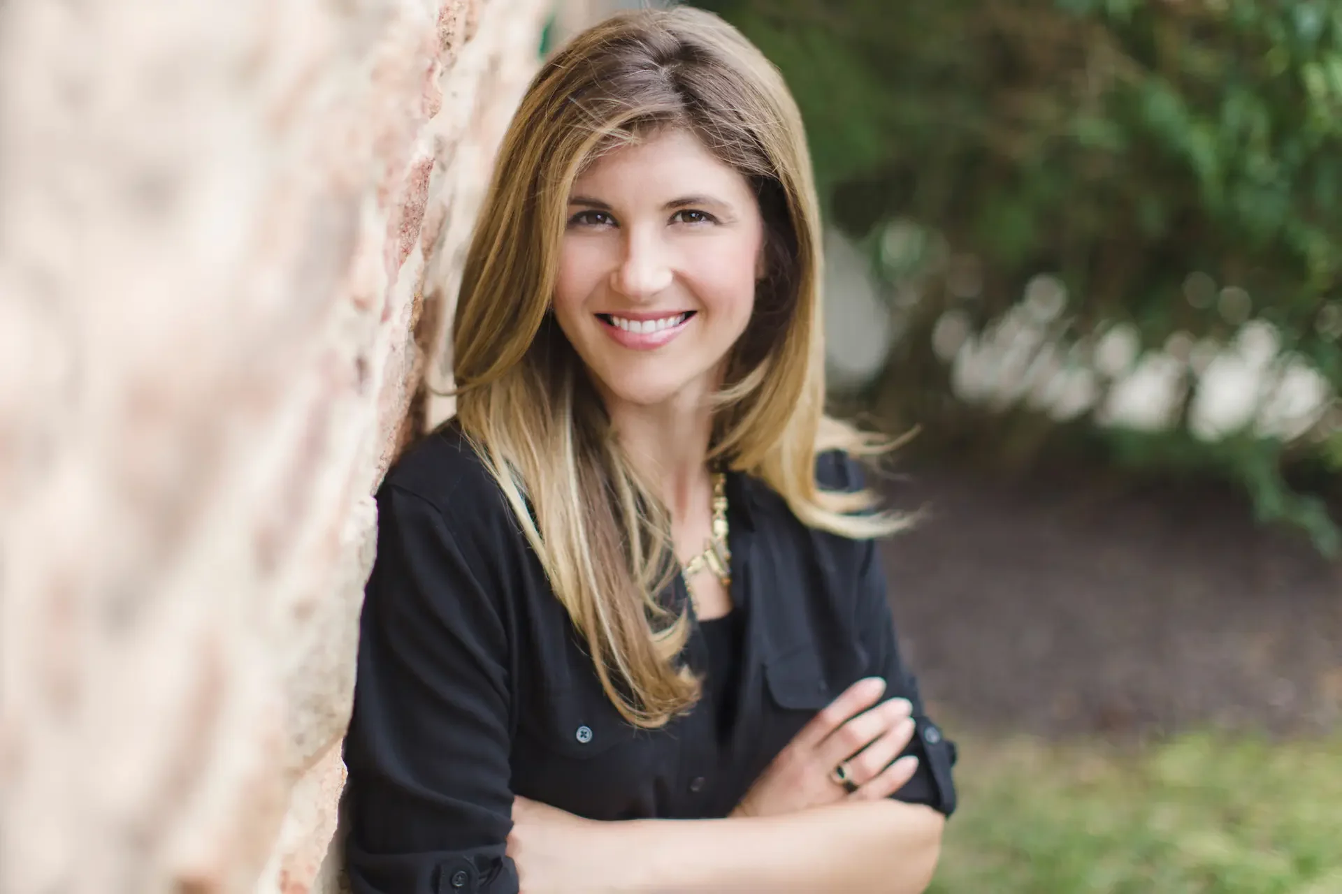 Deborah Pauletta: smiling and standing outdoors next to a brick wall, with greenery in the background. Therapist at Edith Schatz LLC