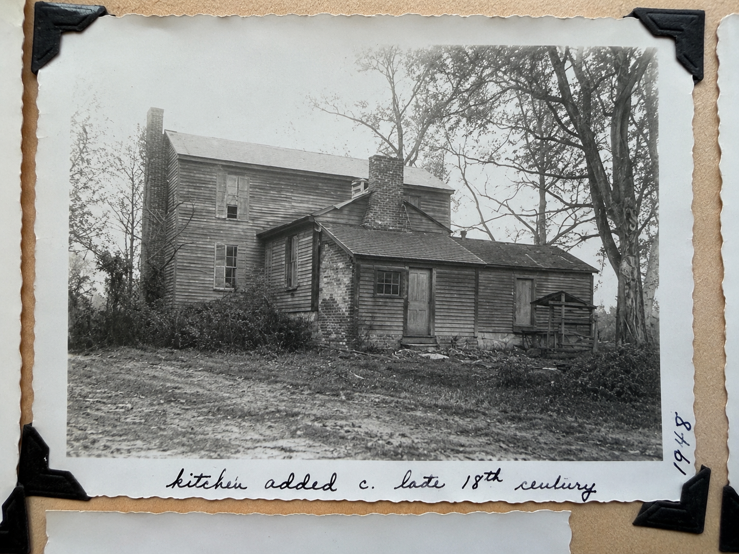 Black and white photo of an old wooden house, with a brick chimney, surrounded by trees, and a dirt path in the foreground. The photo has handwritten notes at the bottom reading 'kitchen added c. late 18th century' and the date 1918.