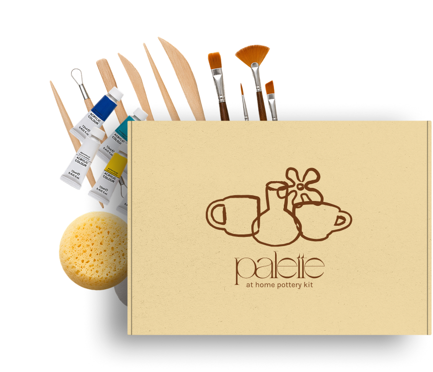 A home pottery kit with various paint brushes, acrylic paint tubes, a sponge, and a cardboard box with a logo of pottery cups and the words "palette at home pottery kit."
