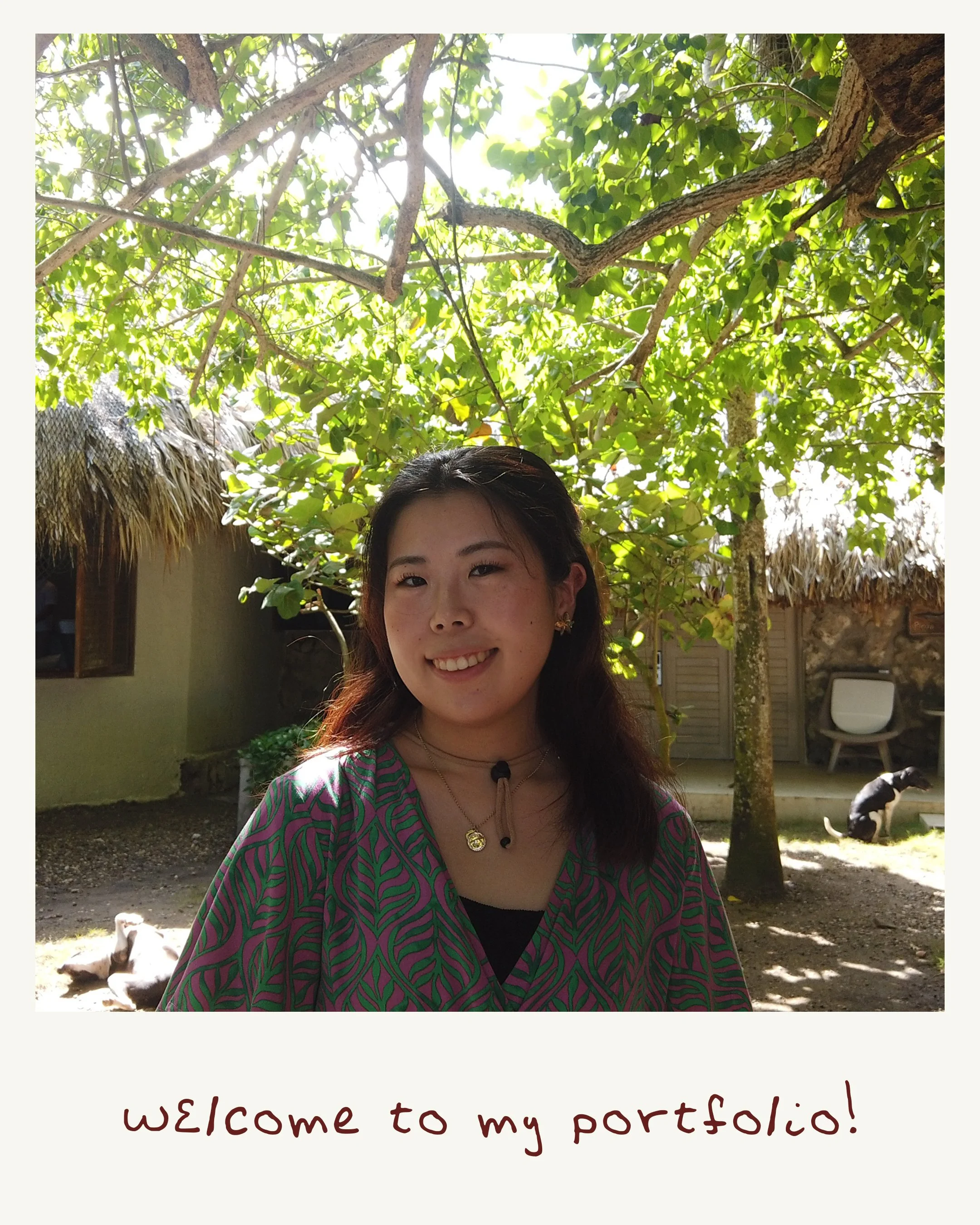 A young woman smiling outdoors, wearing a colorful patterned top and jewelry, with trees in the background. The bottom of the image features a white border with handwritten-style text that reads, 'welcome to my portfolio!'