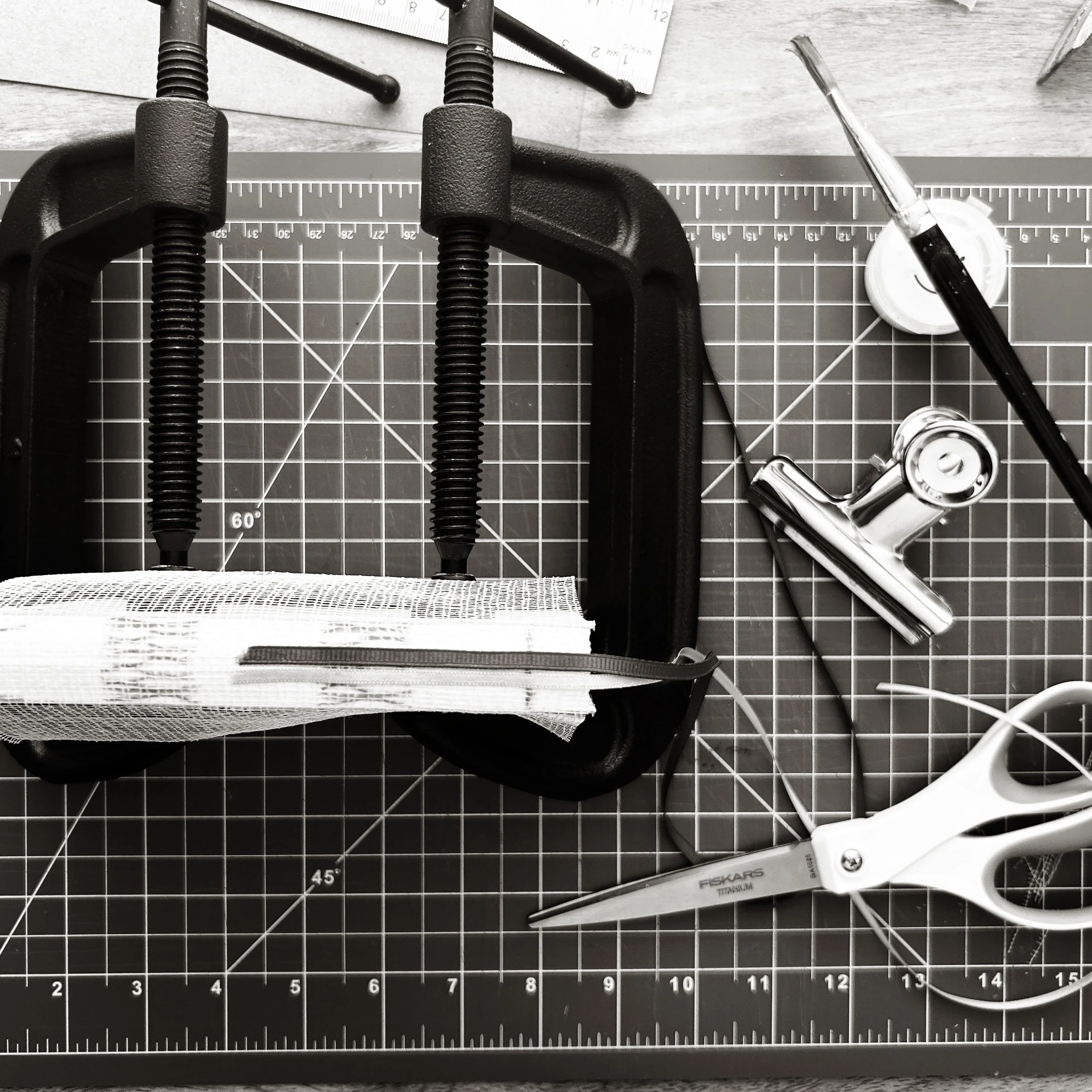 A C-clamp, a ruler, a screwdriver, a wrench, and other tools on a work surface with a cutting mat.