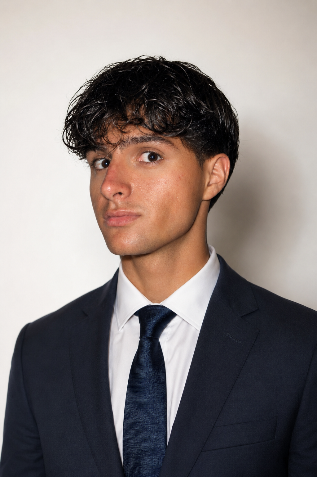 Young man in a suit with dark hair and fair skin, looking at the camera, against a plain light background.