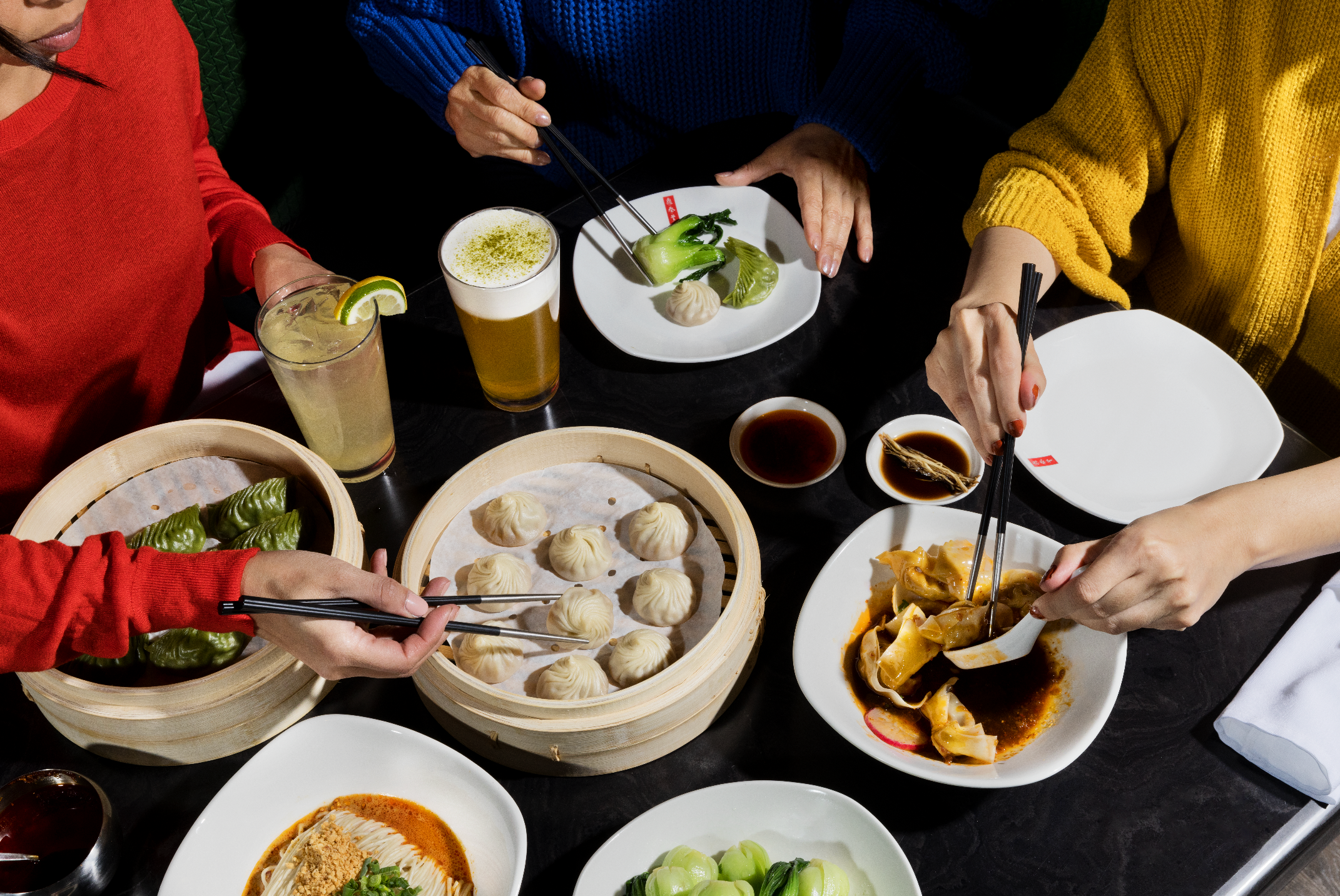 Spread of different Taiwanese foods such as Xiao Long Bao, dumplings, and bok choy with 2 women eating