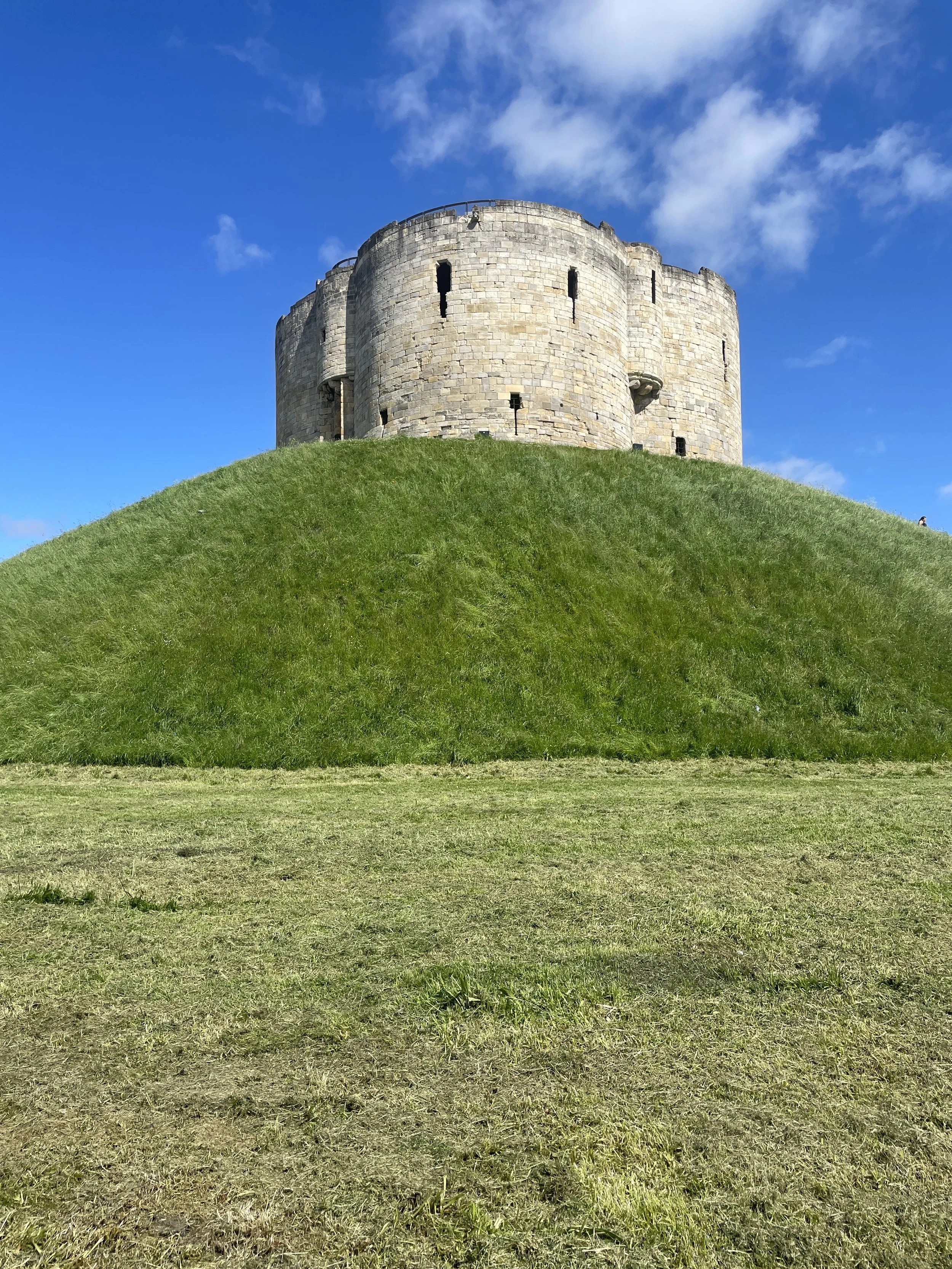 A stone castle on a hilltop against a blue sky with some clouds.